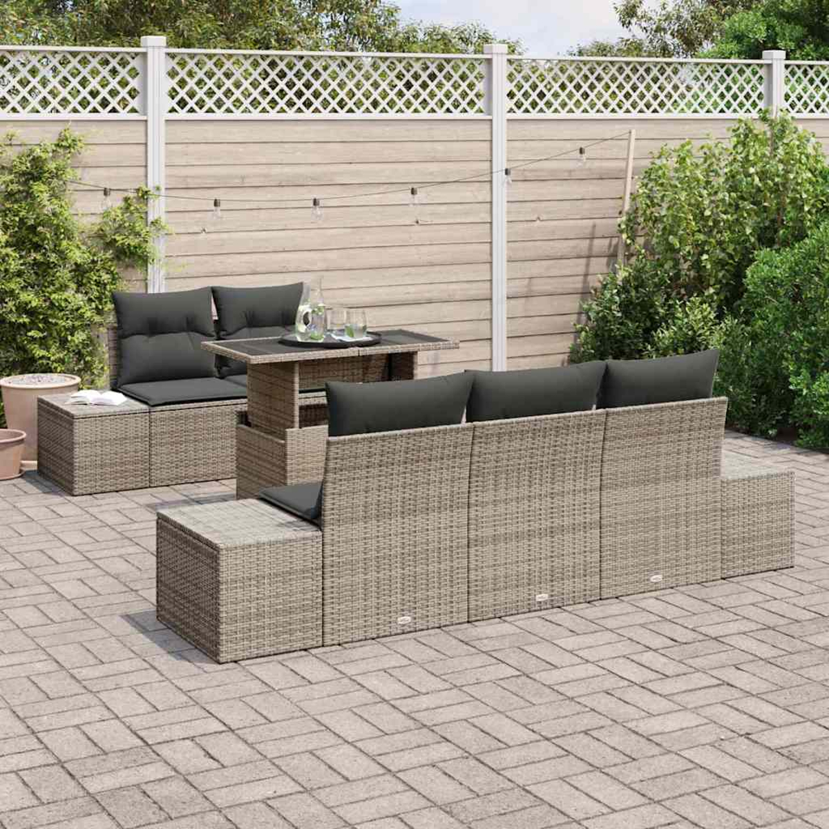 Outdoor-Terrassenset mit grau gewebtem Sofa, Tisch und Stühlen. Auf einer Ziegelterrasse. Ein Holzzaun und Grün im Hintergrund.