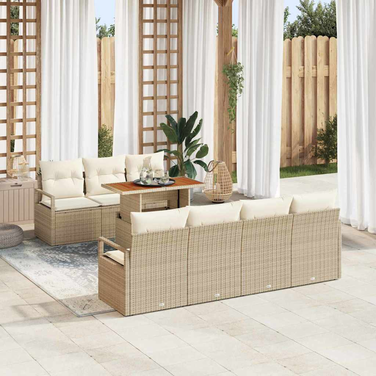 Terrasse im Freien mit beigen Korbsesseln, einem Holztisch und weißen Vorhängen. Grüne Pflanzen und ein Holzzaun im Hintergrund.