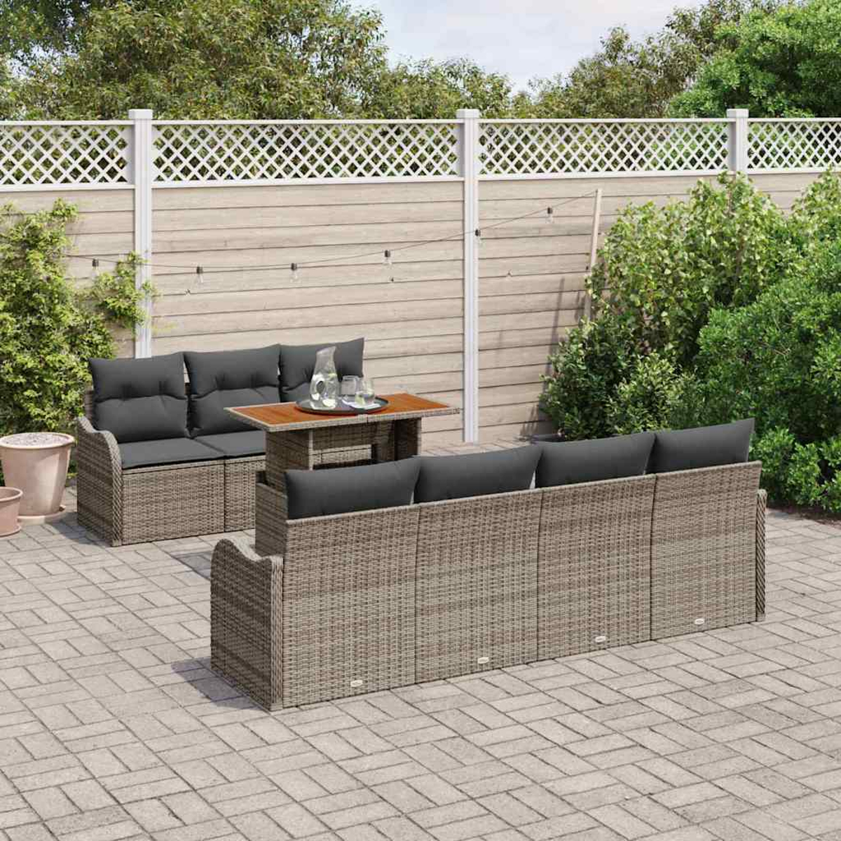 Szene im Freien mit Rattan-Sofa, Tisch und Kissen. Im Hintergrund ein Zaun und Grün. Eine entspannende Umgebung im Freien.