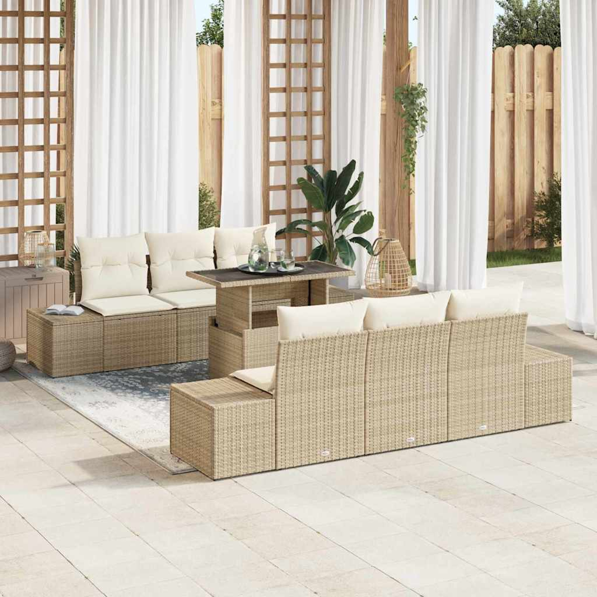 Rattan-Gartenmöbel-Set mit cremefarbenen Kissen, einem Tisch mit Hubfunktion und weißen Vorhängen. Pflanzen und ein Holzzaun im Hintergrund.