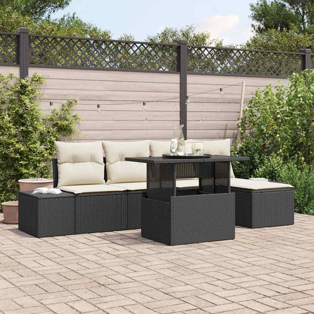 Terrassengarnitur mit schwarzen Korbmöbeln, beigefarbenen Kissen, einem Glastisch und einer Ziegelterrasse, umgeben von Grün und einem Zaun.