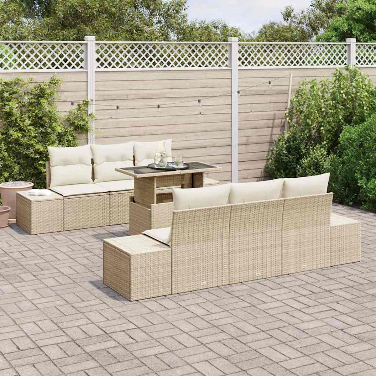 Outdoor-Wicker-Möbelset auf einer Terrasse. Enthält Sofa, Stühle und einen Tisch mit cremefarbenen Kissen. Im Hintergrund ein Zaun und Grün.
