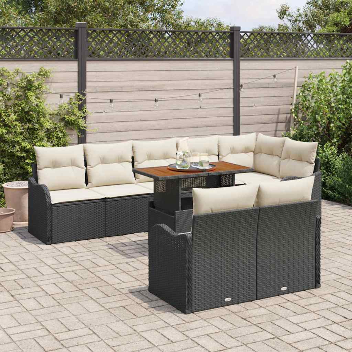 Garten-Terrassenset mit schwarzen Korbmöbeln, beigen Kissen und einem Holztisch. Im Hintergrund sind ein Zaun und Grün zu sehen.