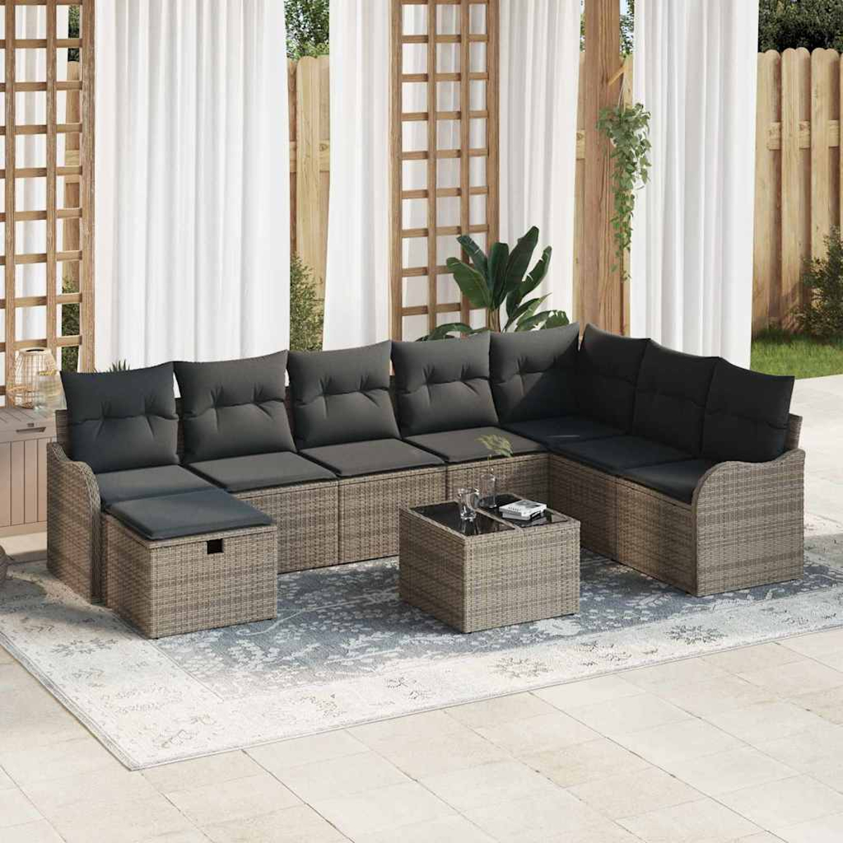 Outdoor-Ecksofa mit grauen Kissen auf einem gemusterten Teppich. Ein quadratischer Tisch und weiße Vorhänge im Hintergrund.