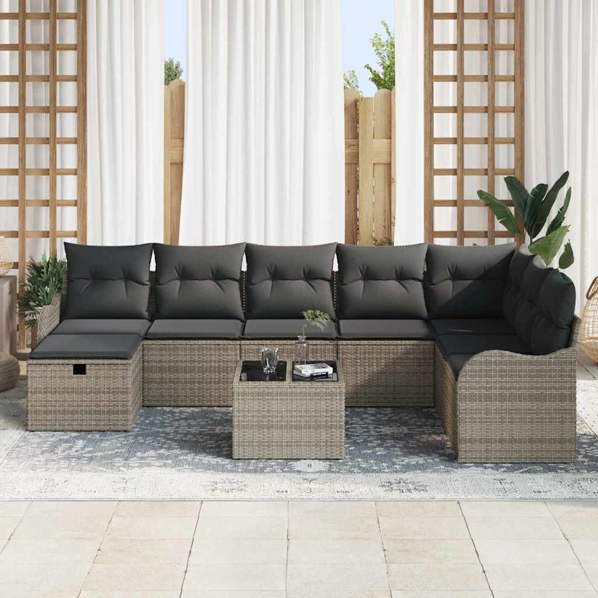 Outdoor-Ecksofa mit grauen Kissen auf einer Terrasse. Vor dem Sofa steht ein kleiner Tisch mit Gläsern. Weiße Vorhänge im Hintergrund.