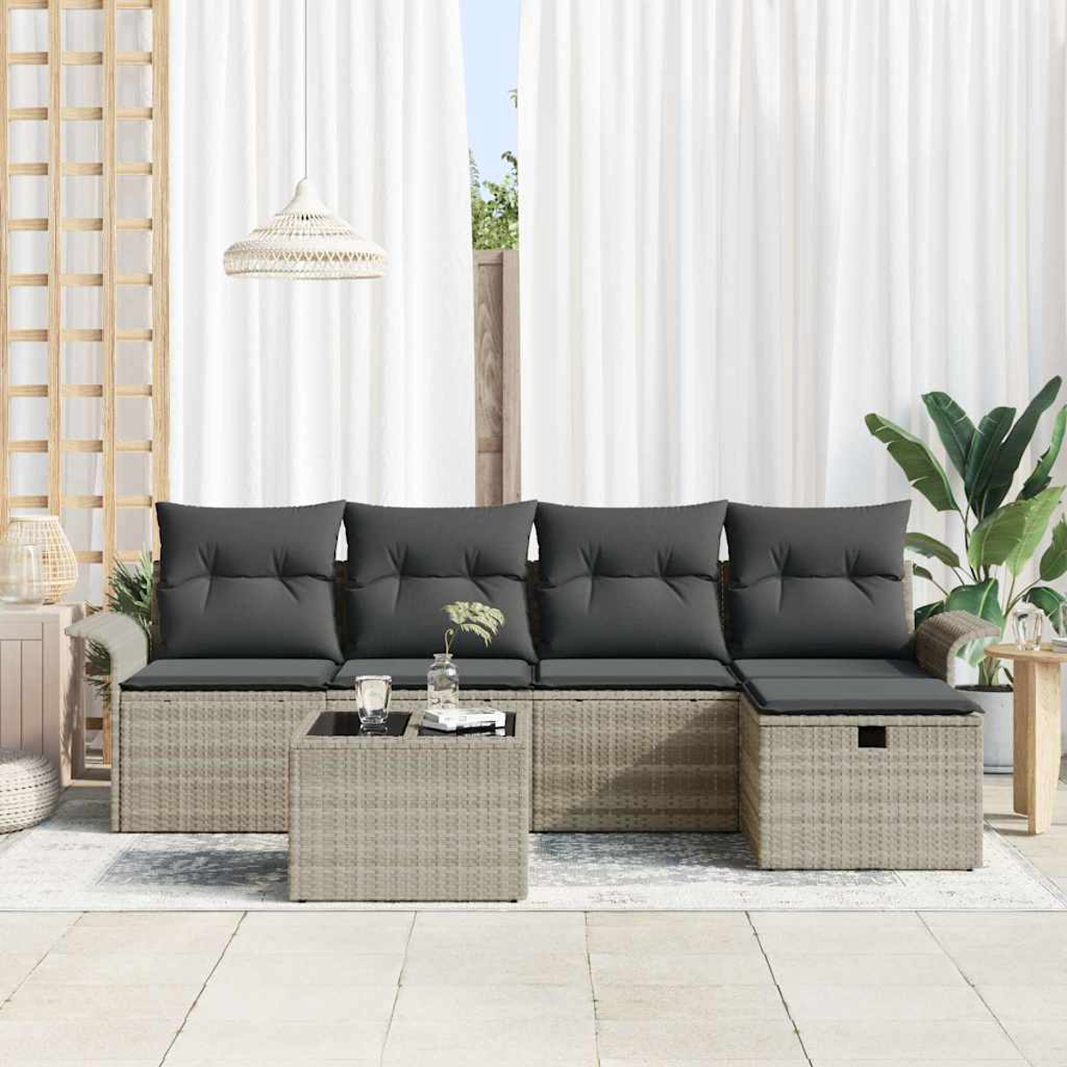 Rattan-Sofa im Freien mit grauen Kissen, einem Couchtisch und einer Pflanze, vor weißen Vorhängen und hellem Holz.