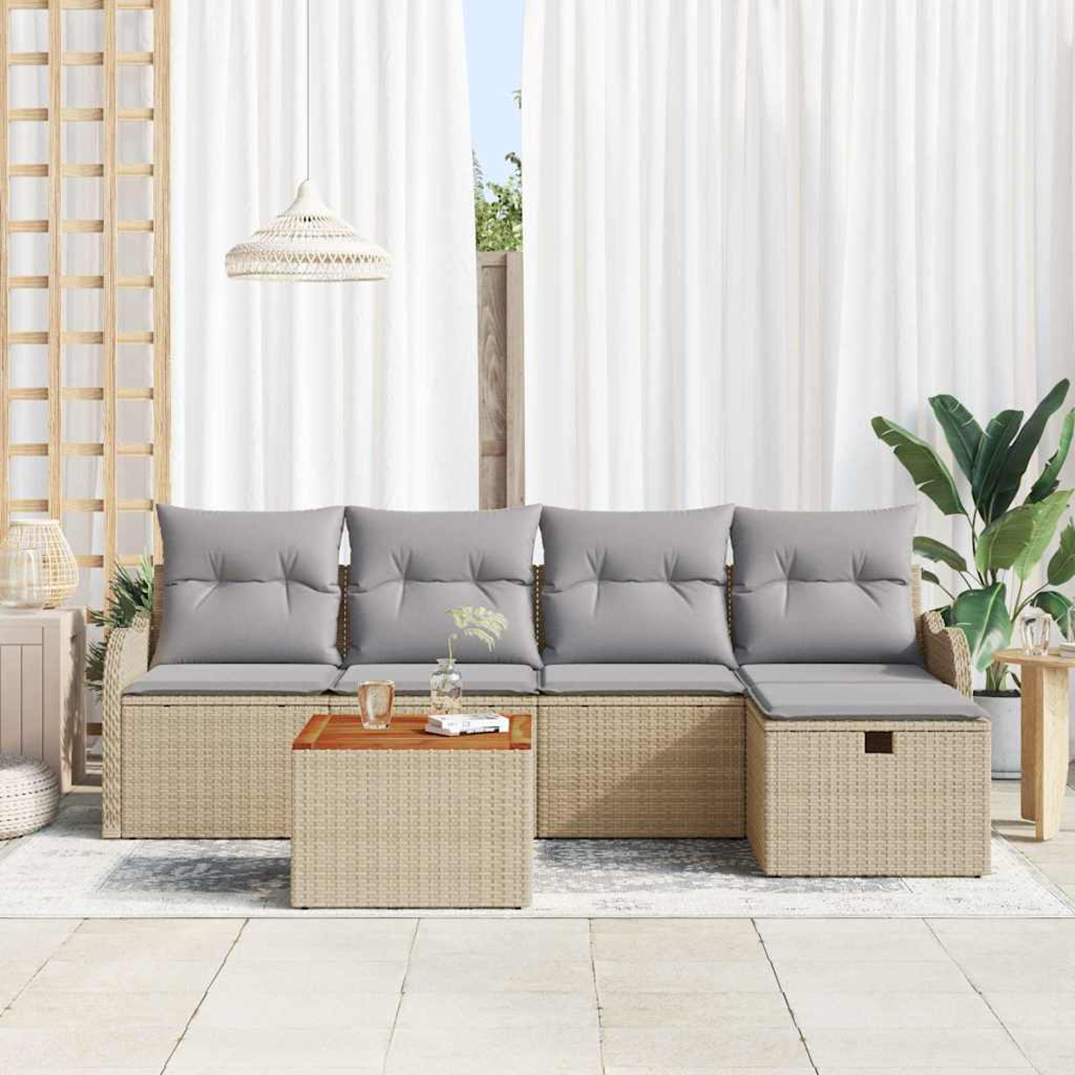 Ein hellbeige Rattan-Sofa mit grauen Kissen und einem Holztisch steht auf einer Terrasse. Weiße Vorhänge und Pflanzen sind im Hintergrund.