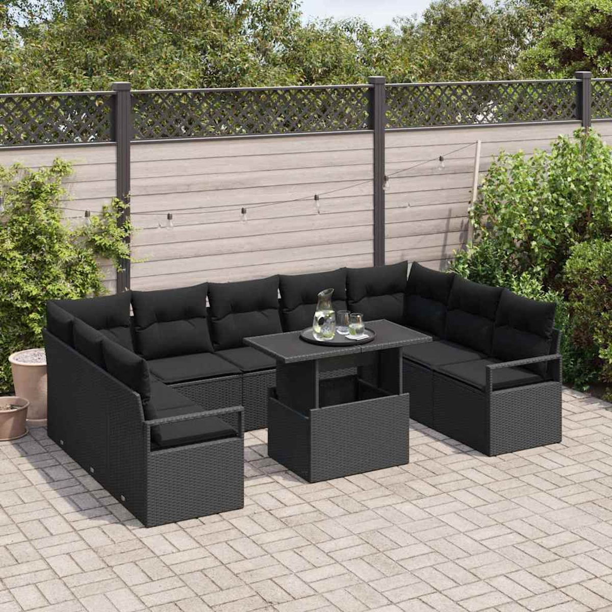 Schwarzes Outdoor-Ecksofa mit Kissen und Tisch auf einer Terrasse. Auf dem Tisch stehen ein Krug und Gläser.
