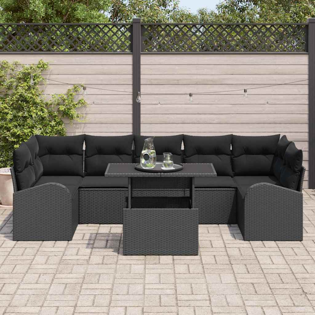 Graues Outdoor-Ecksofa mit schwarzen Kissen und einem Tisch auf einer Terrasse. Im Hintergrund befinden sich ein Zaun und Grün.