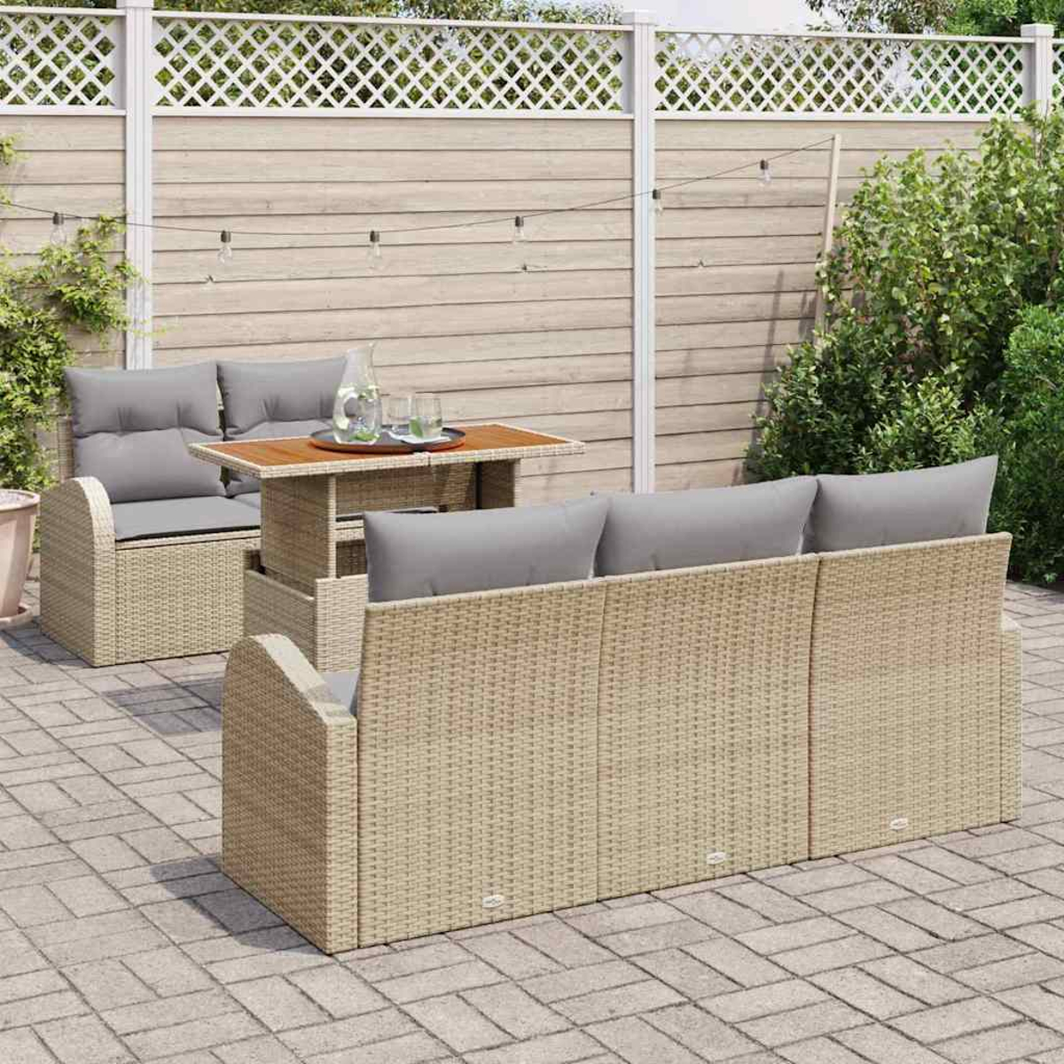 Gartenmöbel-Set aus Korbgeflecht mit grauen Kissen, einem Holztisch und einem weißen Zaun im Hintergrund.