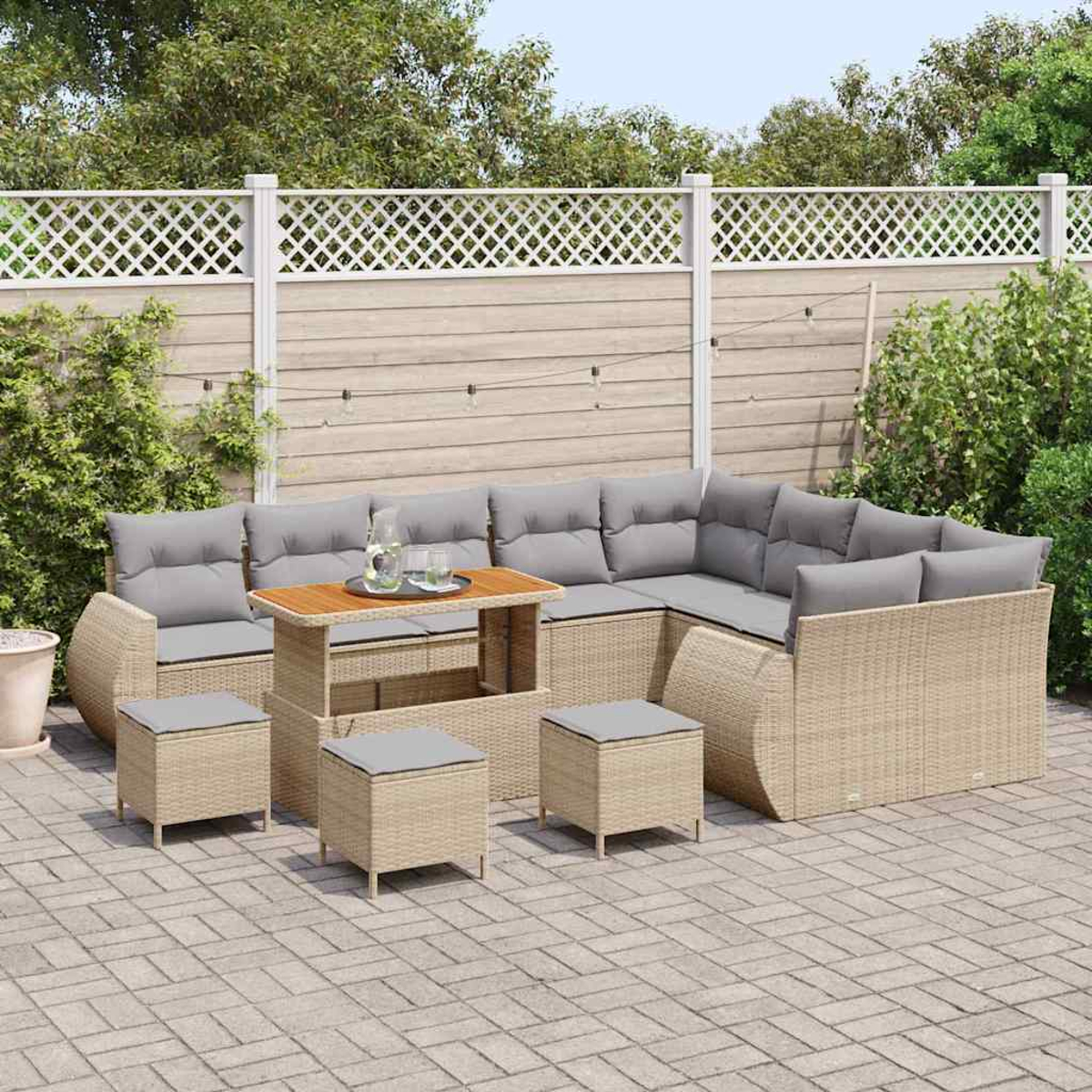 Outdoor-Rattansofa-Set mit grauen Kissen, Couchtisch und Hockern auf einer Backsteinterrasse vor einem Holzzaun.