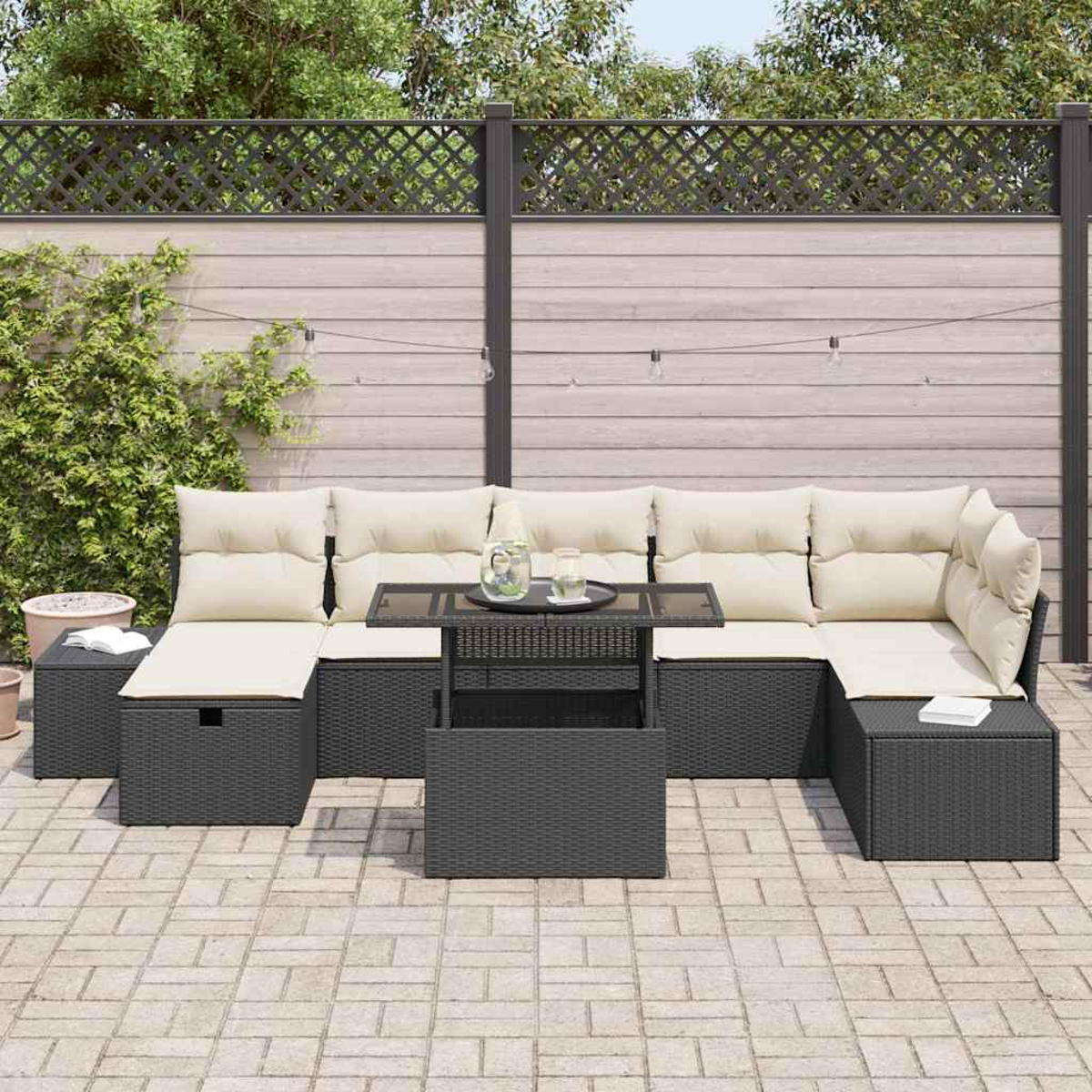 Outdoor-Ecksofa mit cremefarbenen Kissen, Tisch mit Glasplatte und Ziegelpflaster. Zierzaun und Laub im Hintergrund.