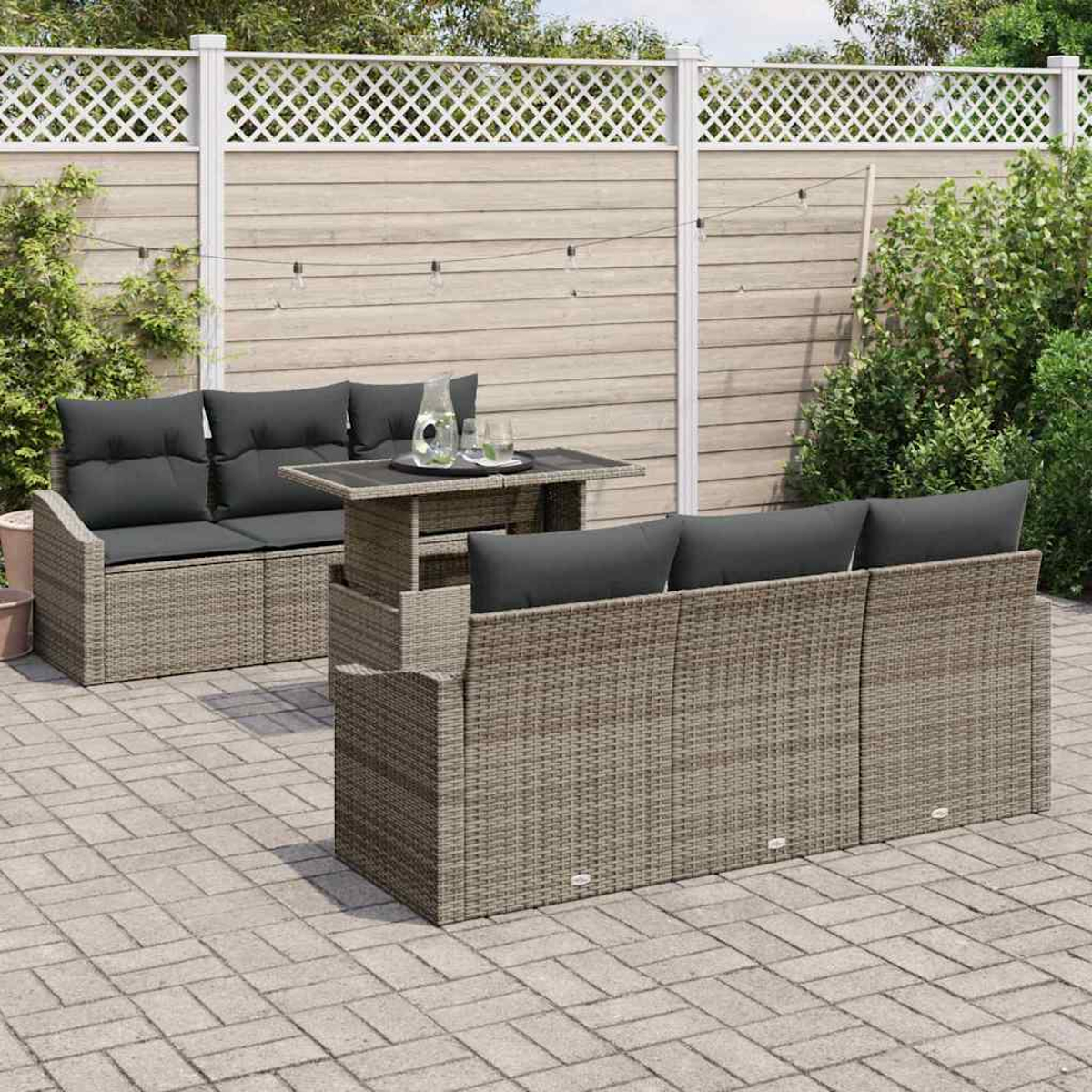 Conjunto de muebles de mimbre para exteriores con cojines grises, mesa y valla decorativa.
