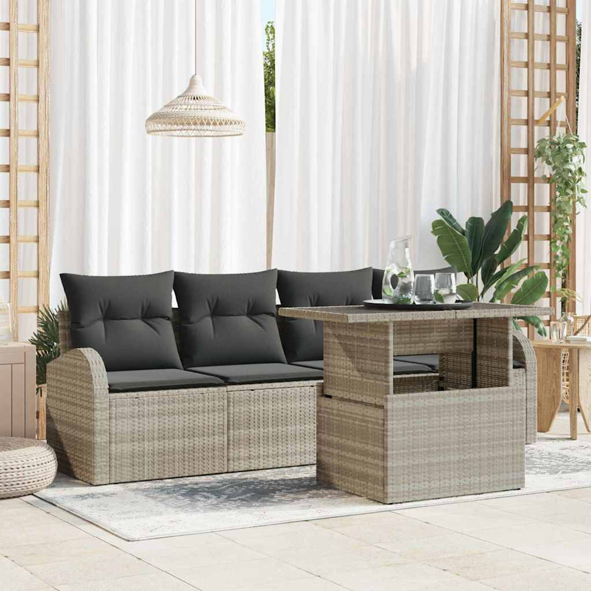 Szene im Freien mit einem Korbmöbel-Sofa, Tisch und Pflanzen. Graue Kissen auf dem Sofa. Weiße Vorhänge und eine Hängelampe im Hintergrund.