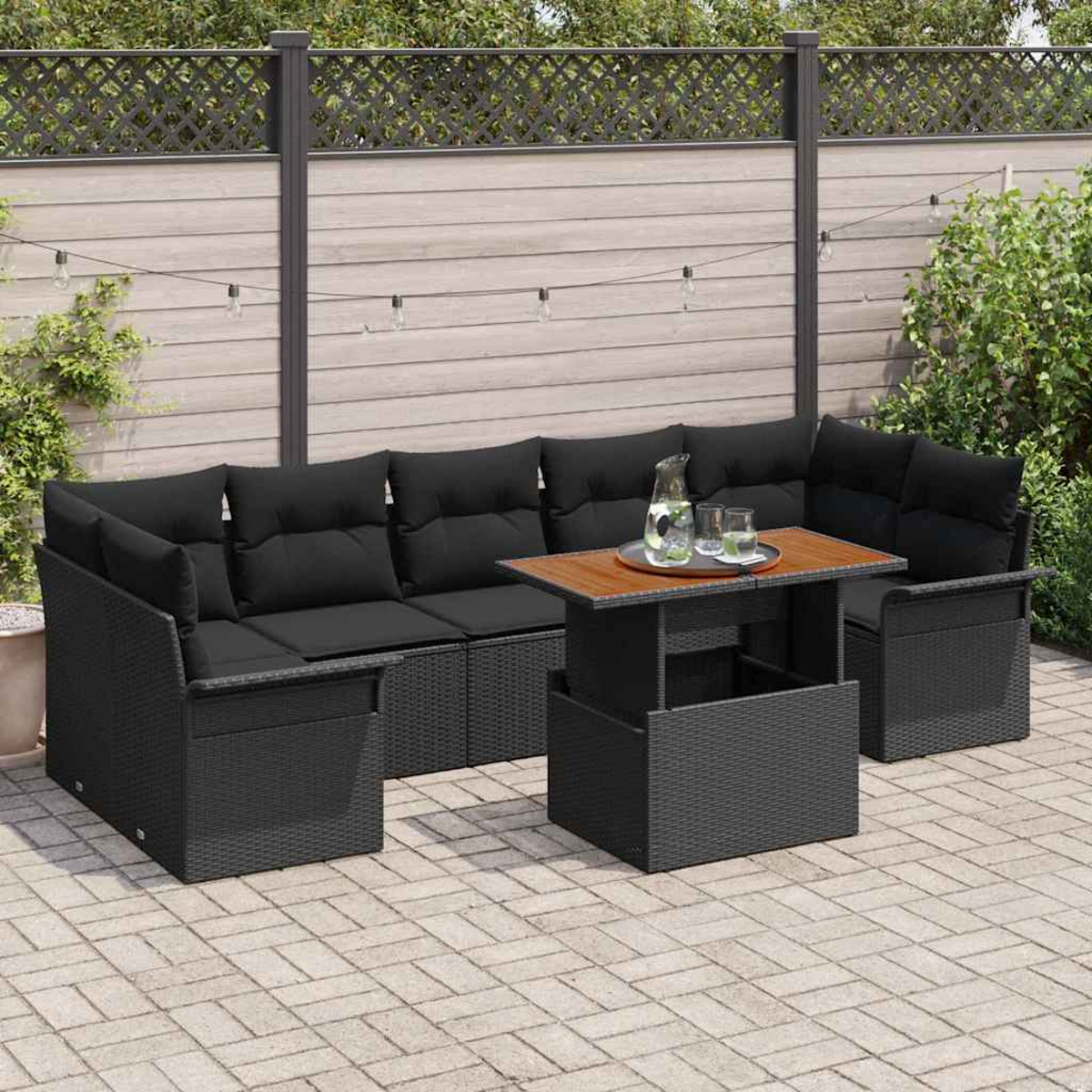 Gartensektionssofa mit schwarzen Kissen und einem Holztisch. Es steht auf einer Terrasse mit Zaun und Lichterketten.