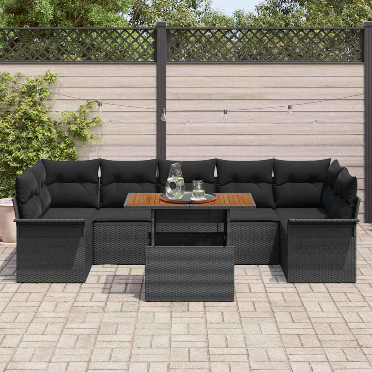 Schwarzes Outdoor-Wicker-Ecksofa mit schwarzen Kissen, Holztisch und dekorativem Zaun im Hintergrund. Pflanzen und Lichter sind sichtbar.