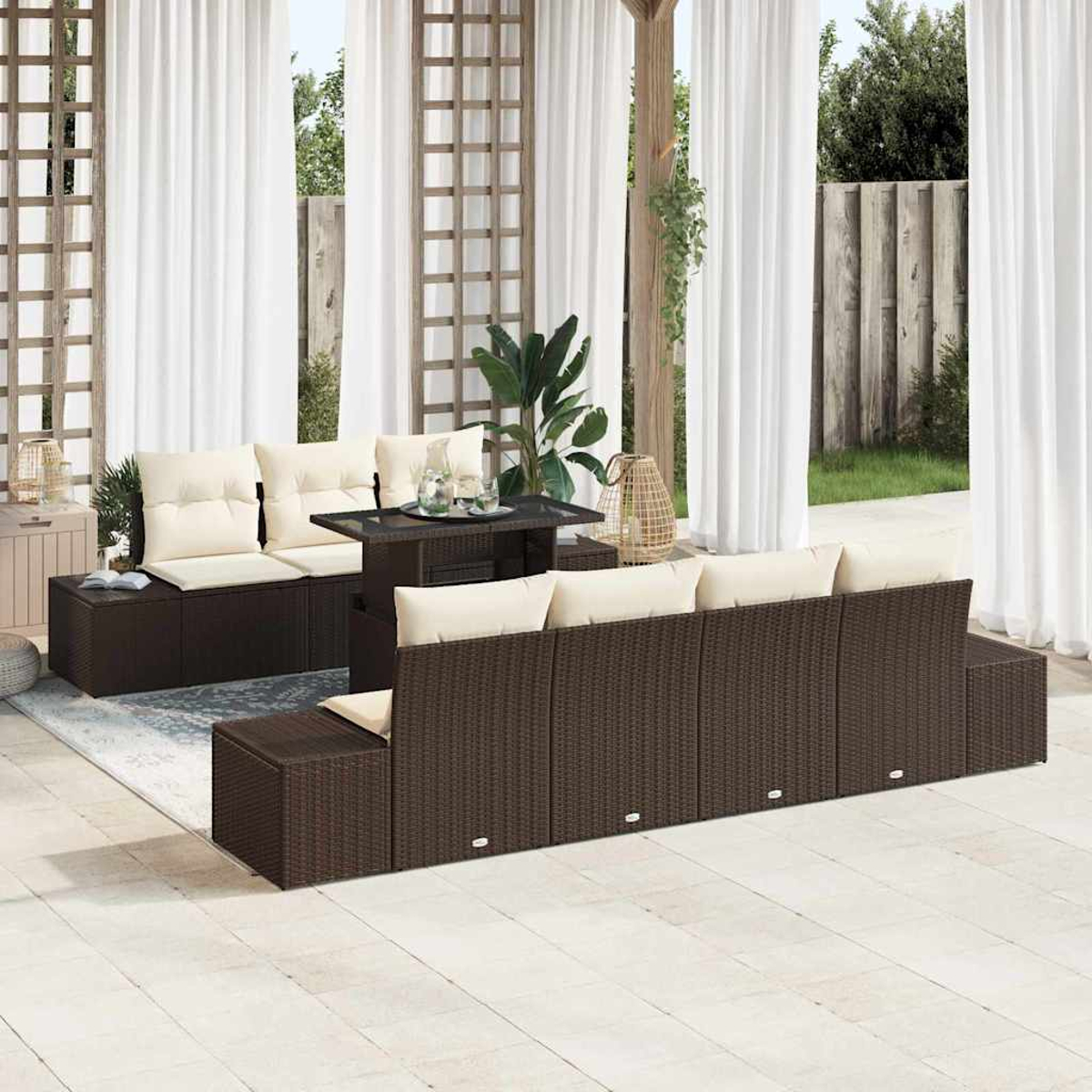 Outdoor-Sitzarrangement mit braunen Korbmöbeln, beigen Kissen und einem Tisch mit Glasplatte. Weiße Vorhänge und Pflanzen im Hintergrund.