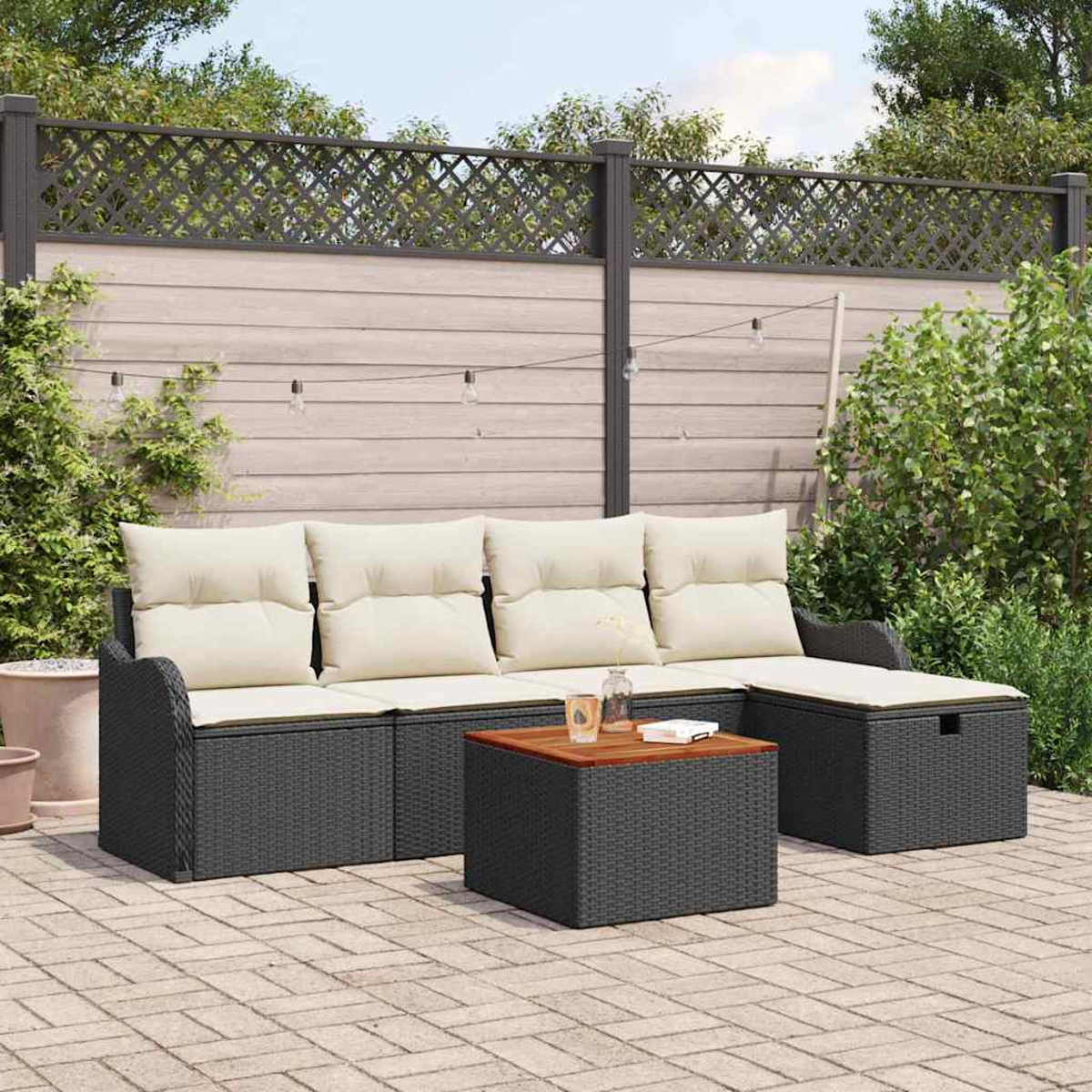 Garten-Terrassenset mit schwarzem Korbmöbel-Sofa und Couchtisch mit Holzplatte. Im Hintergrund ein Zaun und Pflanzen.