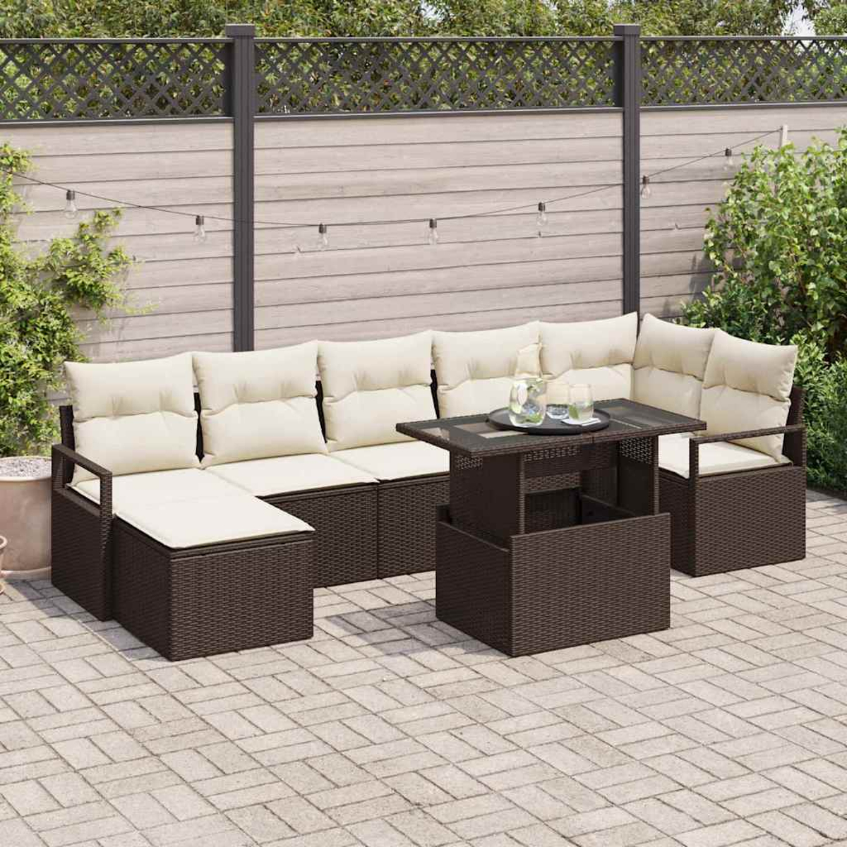Outdoor-Korbsessel mit cremefarbenen Kissen, passendem Couchtisch und Steinpflaster. Im Hintergrund ein Holzzaun.