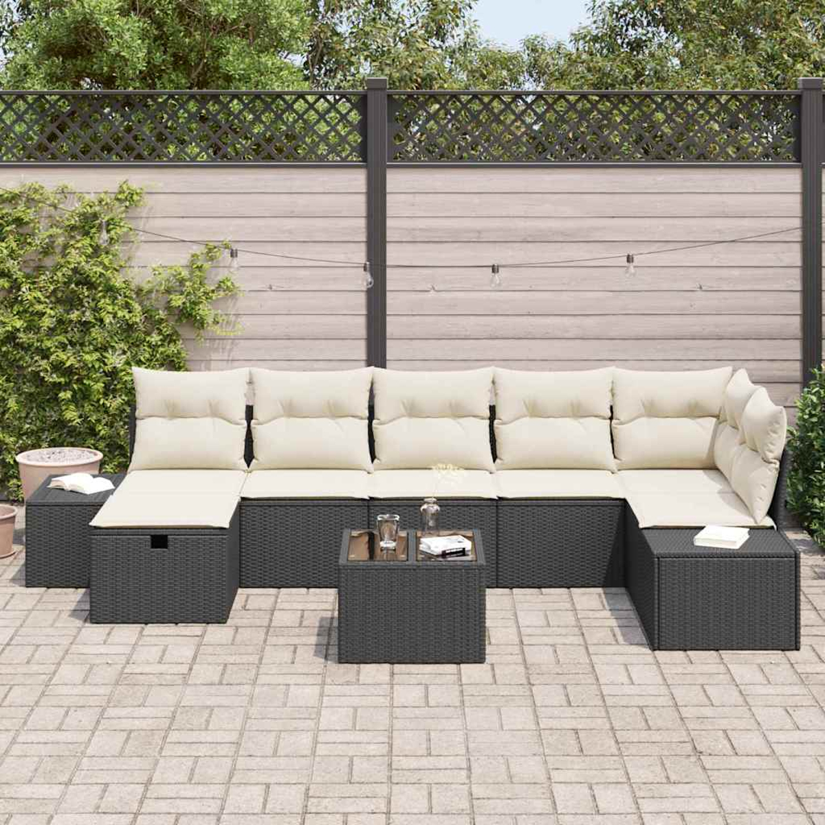 Ein Outdoor-Ecksofa mit cremefarbenen Kissen steht auf einer Ziegelterrasse. Davor steht ein kleiner Tisch mit Gegenständen. Hinten ist ein Holzzaun.