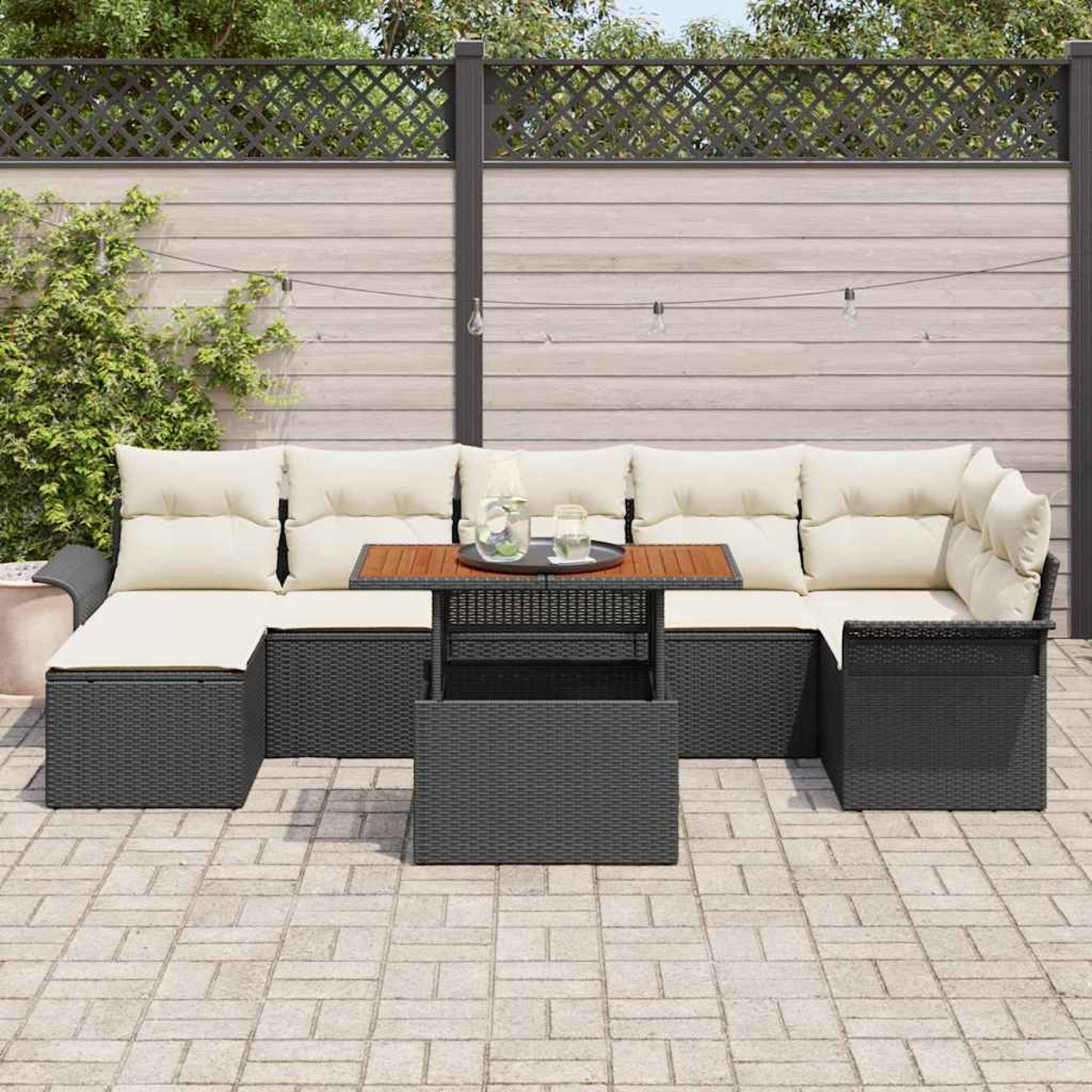 Garten-Sitzgruppe mit cremefarbenen Kissen und schwarzem Korbgewebe. Davor steht ein Tisch mit Holzplatte. Im Hintergrund ein Holzzaun.