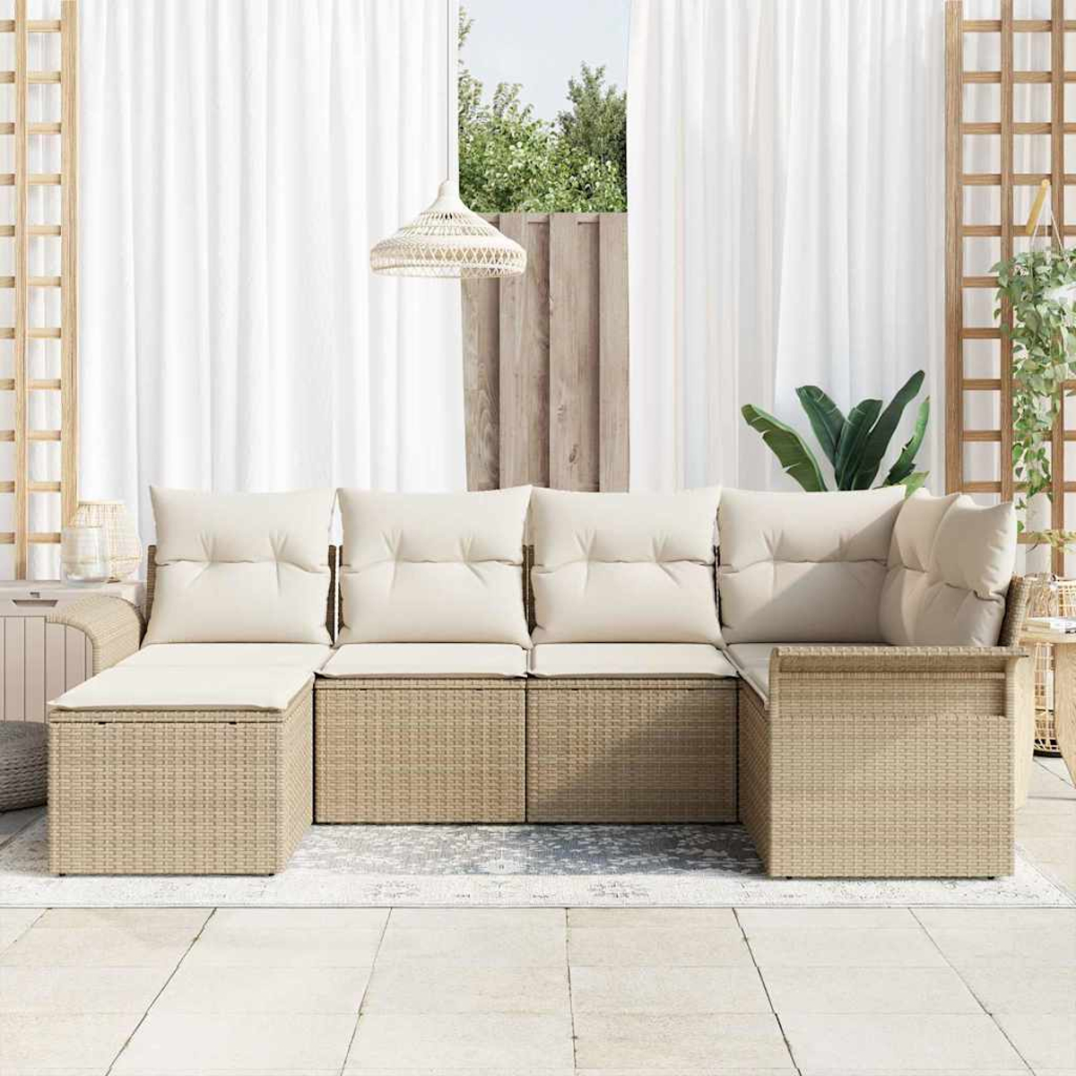 Sofá de mimbre beige para exteriores con cojines crema. Cortinas blancas y una ventana con vegetación al fondo, alfombra neutra en el suelo.
