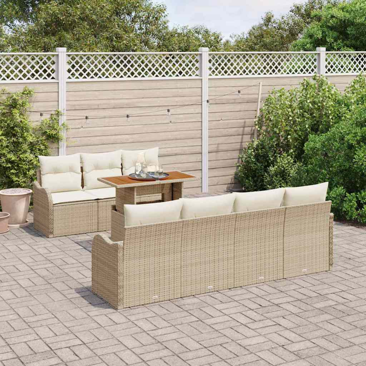 Garten-Wicker-Möbel-Set auf einer Terrasse. Enthält ein Sofa, eine Doppelsitzer und einen Tisch mit Kissen. Hintergrund ist ein Zaun und Grün.