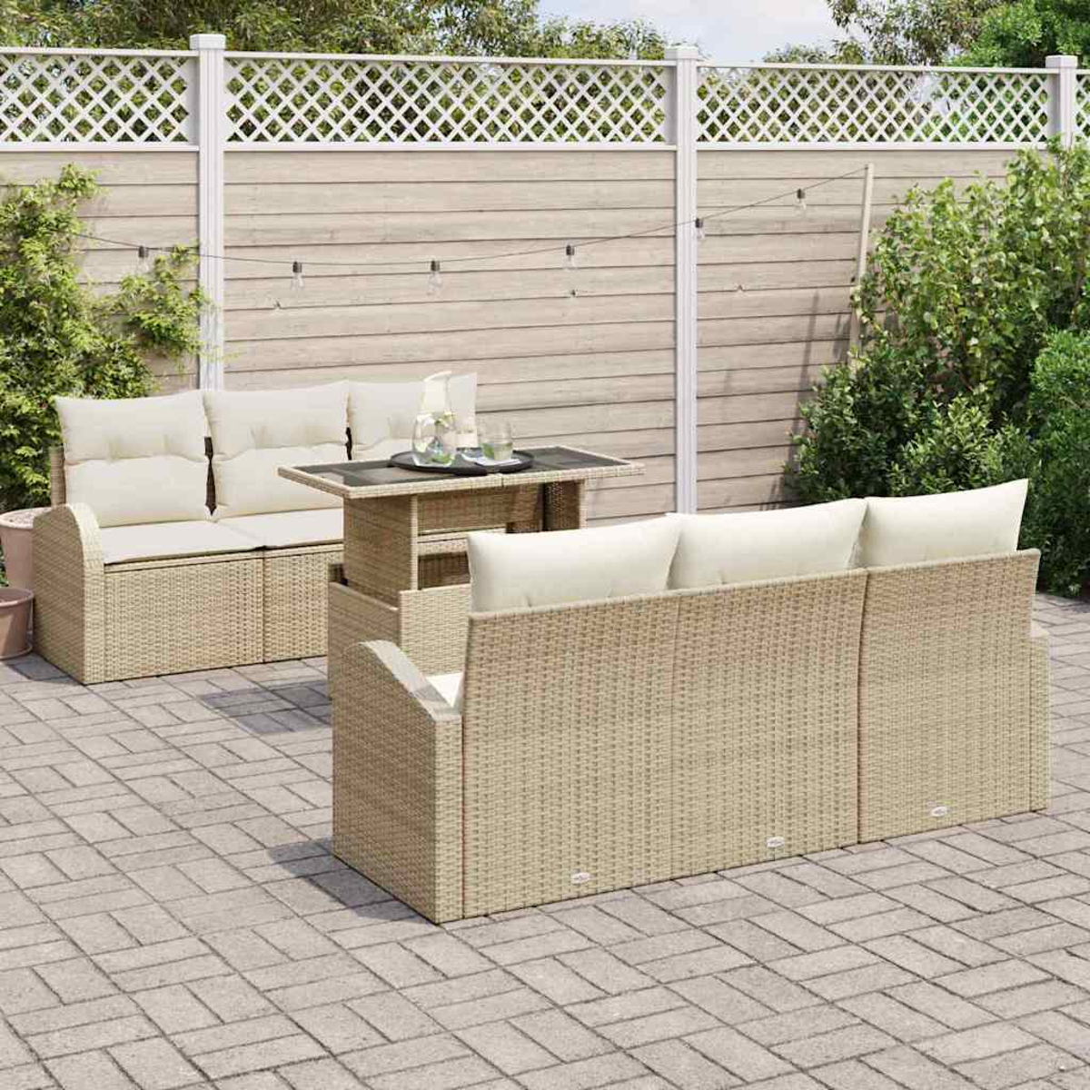 Juego de patio al aire libre con muebles de mimbre beige y cojines crema. Una mesa pequeña con bebidas en el medio. Una valla en el fondo.