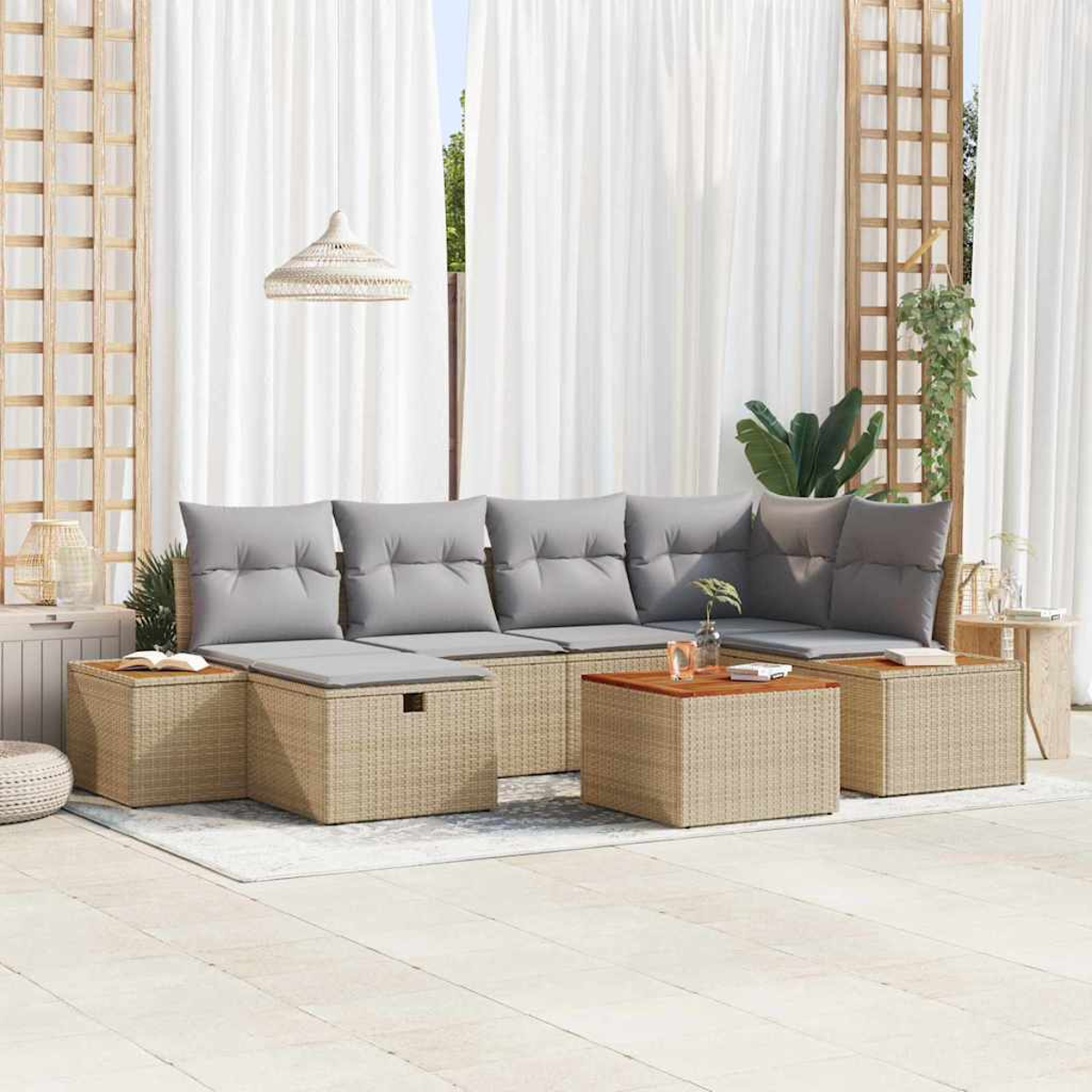Gartenlounge mit grauen Kissen, Korbmöbeln und Holztisch vor weißen Vorhängen und einer Gitterwand.