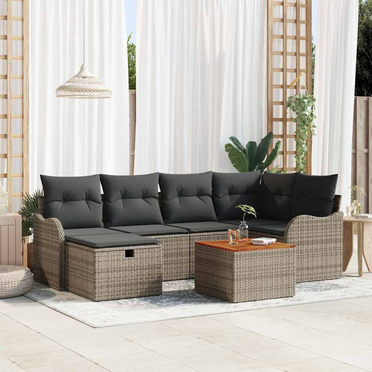 Outdoor-Rattansofa mit grauen Kissen, Couchtisch und weißen Vorhängen. Im Hintergrund sind eine Pflanze und ein dekoratives Gitter zu sehen.