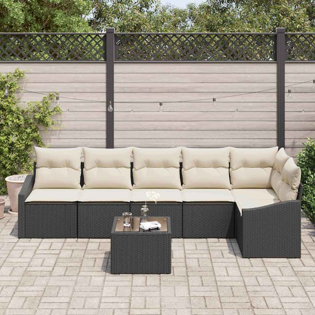 Outdoor-Ecksofa mit beigen Kissen und einem kleinen Tisch auf einer Steinterrasse. Zaun und Grün im Hintergrund.