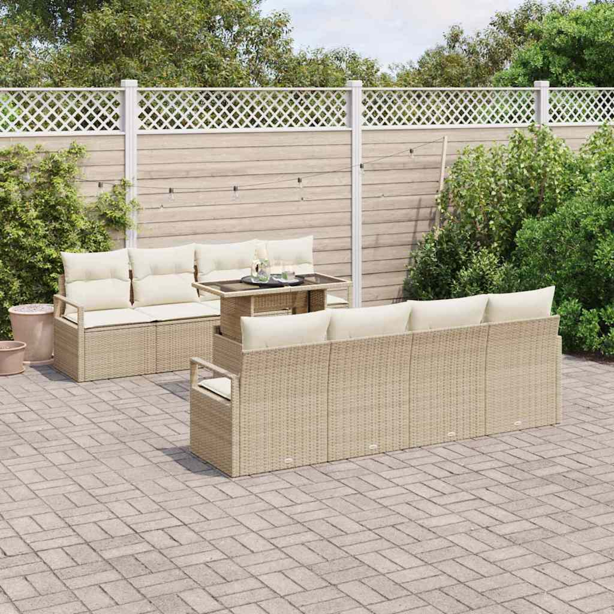 Gartenmöbel-Set aus Korbgeflecht mit Sofa, Zweisitzer und Tisch auf einer gepflasterten Terrasse, vor einem Zaun und Grün.
