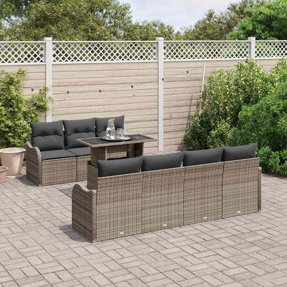 Terrassengarnitur mit Rattansofas und einem Tisch. Graue Kissen und ein Holzzaun im Hintergrund.