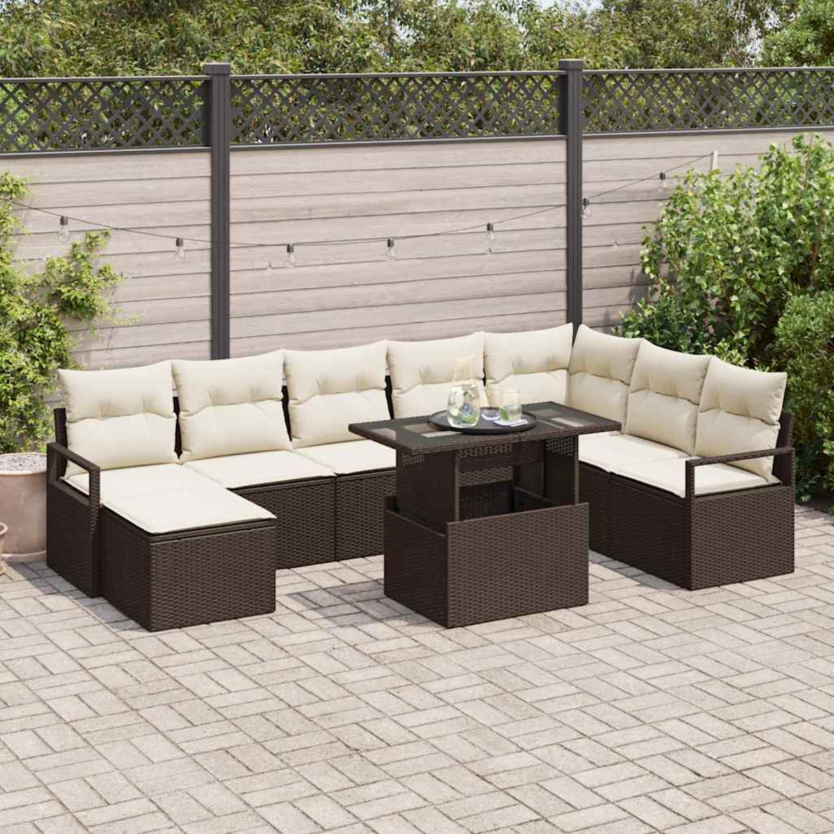 Garten-Set mit braunen Korbmöbeln und cremefarbenen Kissen, einschließlich Tisch, umgeben von Zaun und Pflanzen.