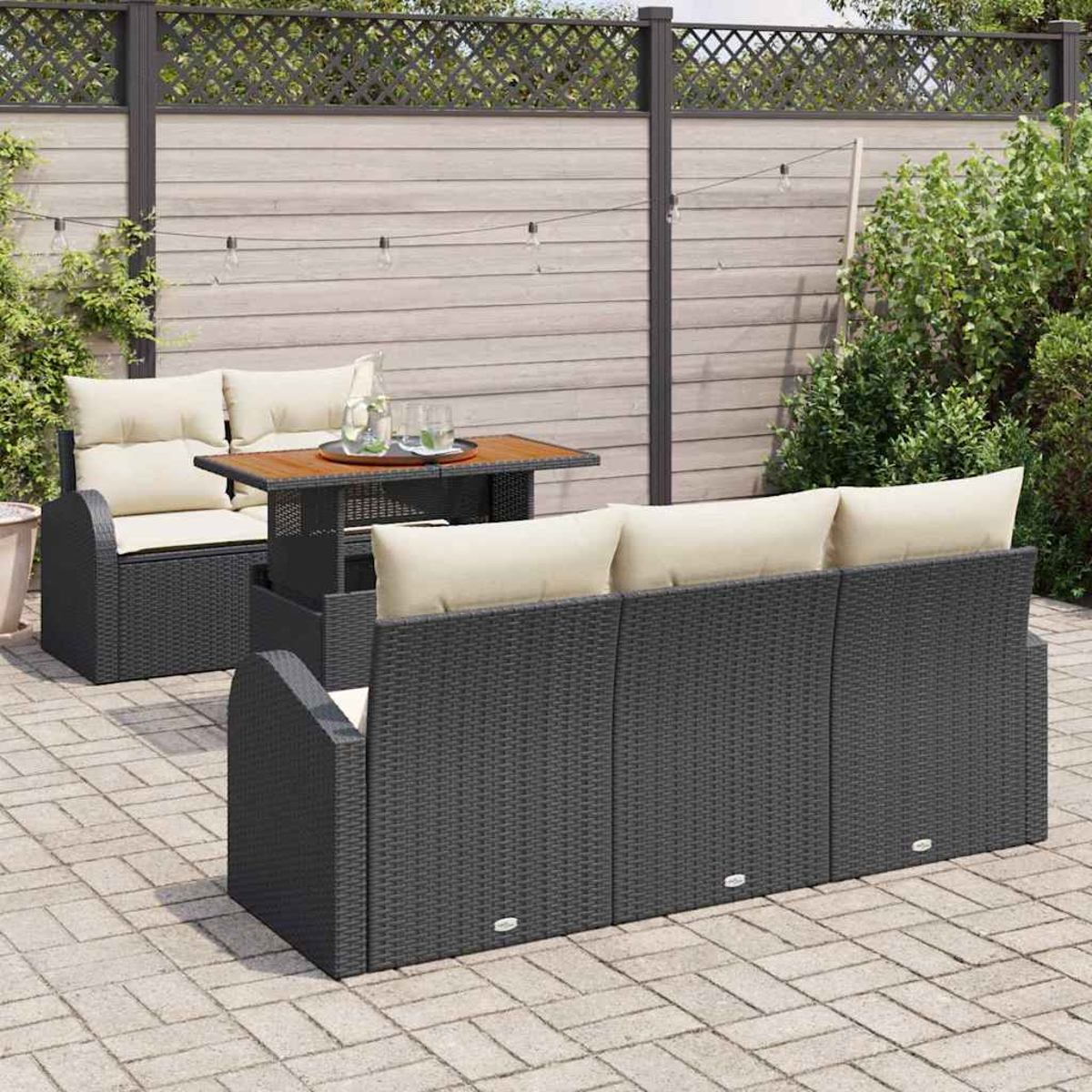 Terrassenset mit dunkelgrauen Korbmöbeln, beigen Kissen und einem Holztisch. Aufgestellt in einem Garten mit Zaun.