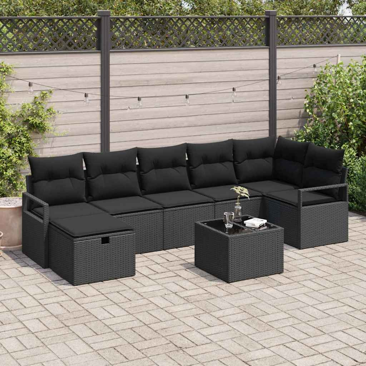 Ein schwarzes Ecksofa mit Kissen und einem kleinen Tisch auf einer Terrasse. Im Hintergrund ein Holzzaun und Pflanzen.