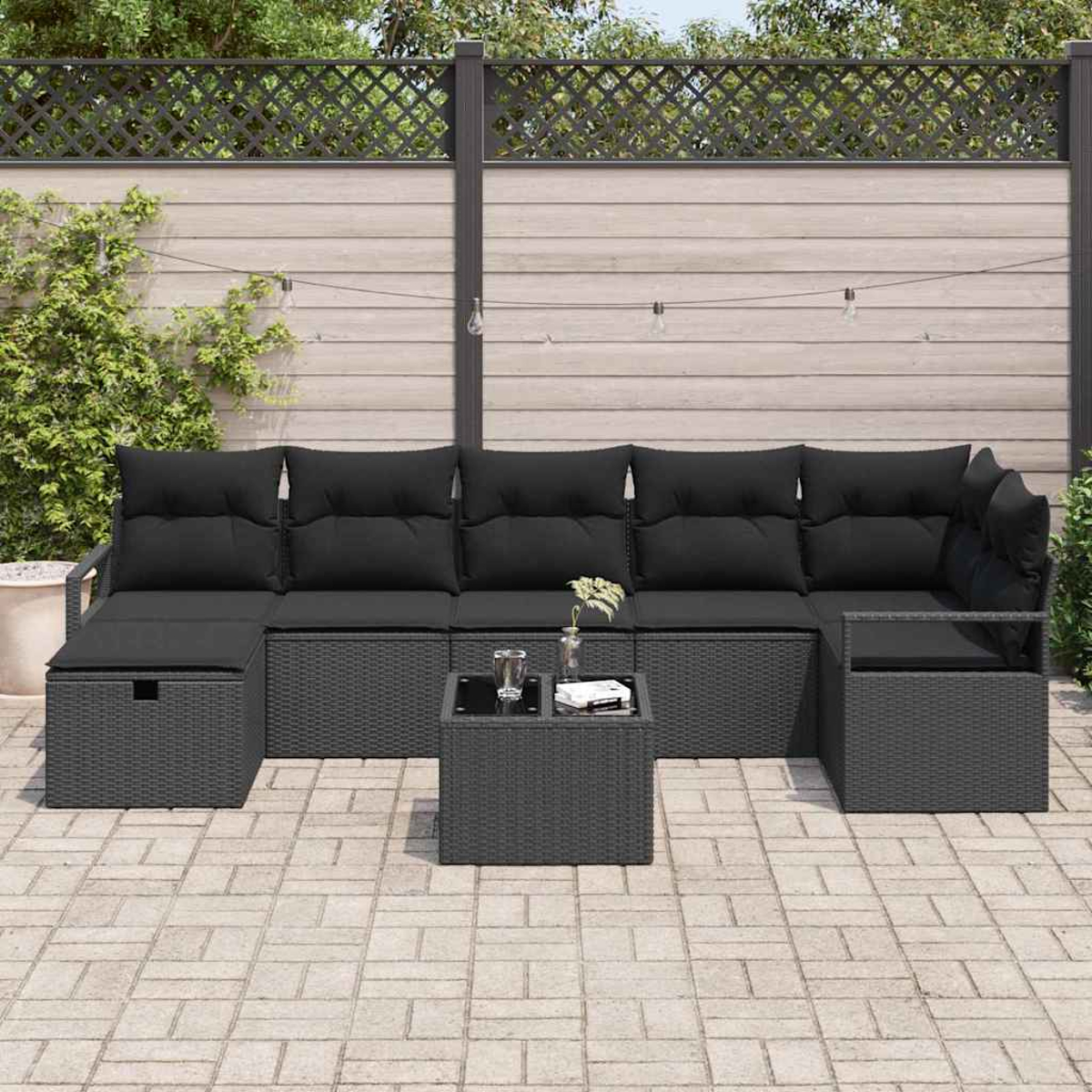 Ein schwarzes Outdoor-Ecksofa mit Kissen und einem kleinen Tisch auf einer Backstein-Terrasse. Im Hintergrund ein Zaun und Pflanzen.