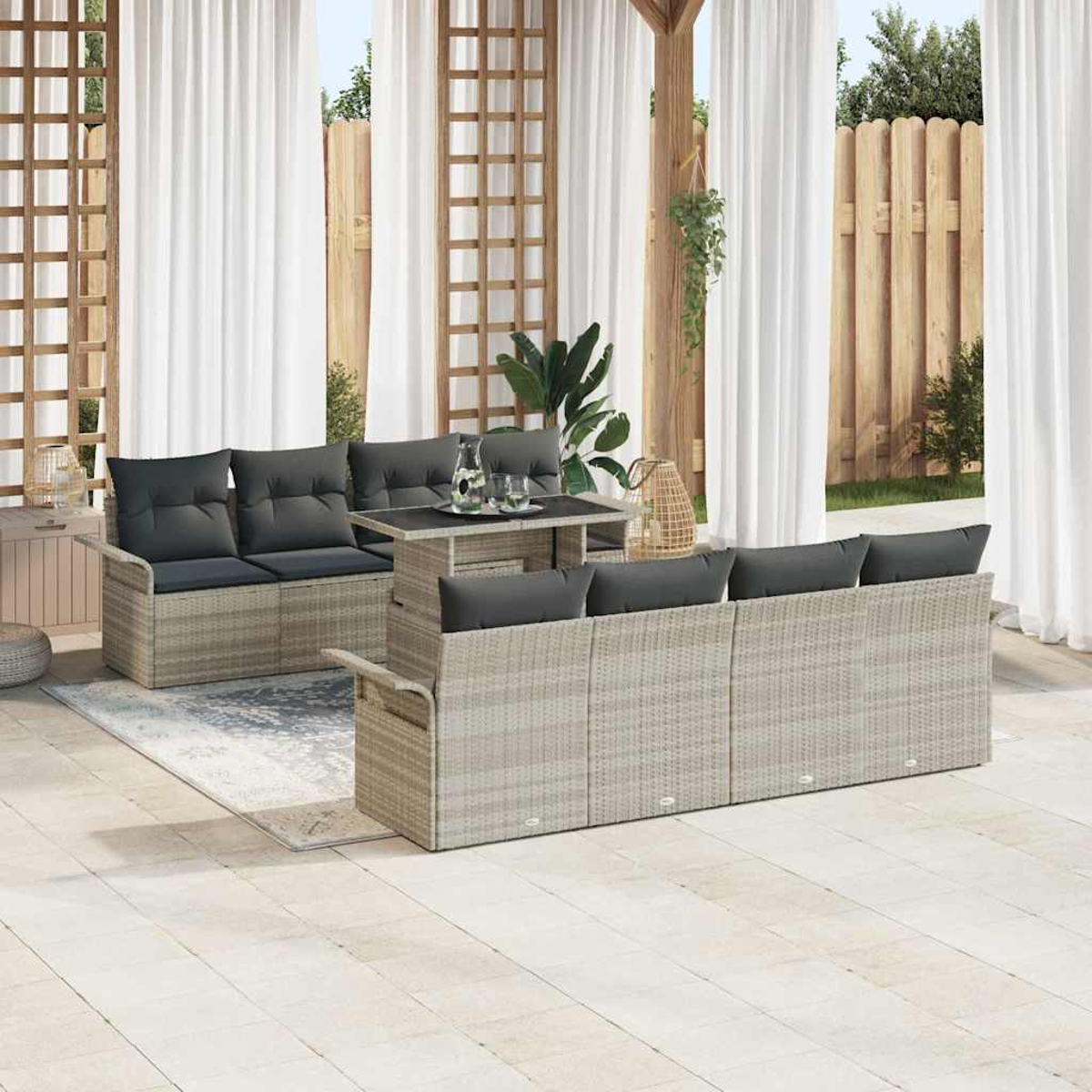 Outdoor-Sitzgruppe mit Tisch, Sofas und Vorhängen. Die Möbel sind hell, mit dunklen Kissen. Im Hintergrund ein Zaun und Pflanzen.