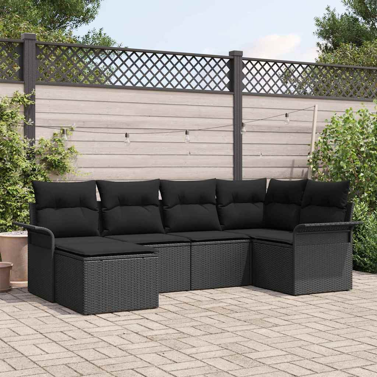 Ein schwarzes Korbsessel-Sofa mit schwarzen Kissen steht auf einer Backstein-Terrasse. Ein Holzzaun und grünes Laub sind im Hintergrund.