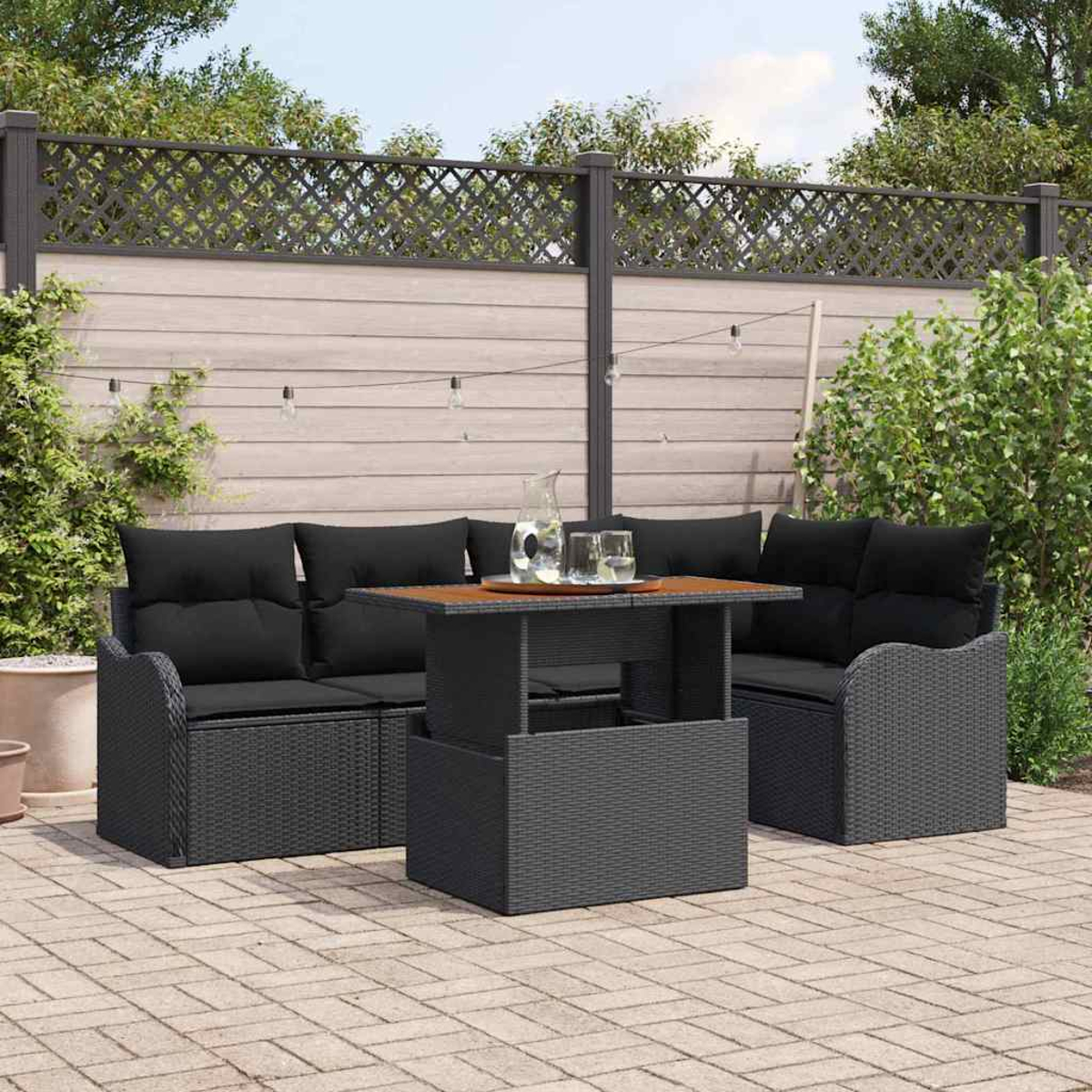 Terrassenset im Freien mit schwarzen Kissen, einem Tisch mit Holzplatte und einem Zaun im Hintergrund.