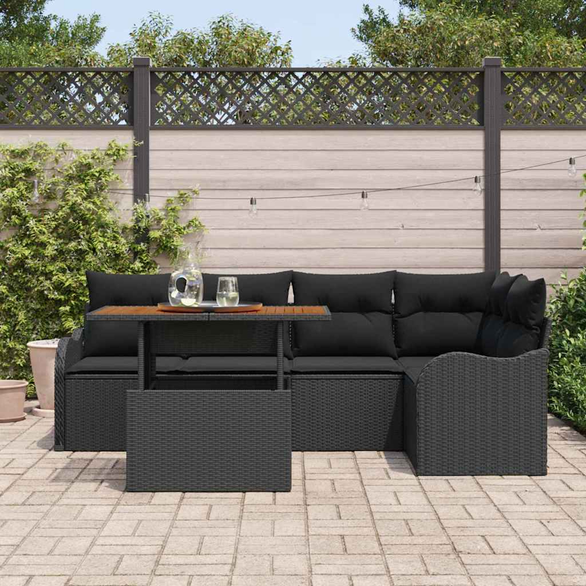 Garten-Terrassengarnitur: schwarzes Korbssofa mit schwarzen Kissen und einem Holztisch, im Hintergrund ein Holzzaun.