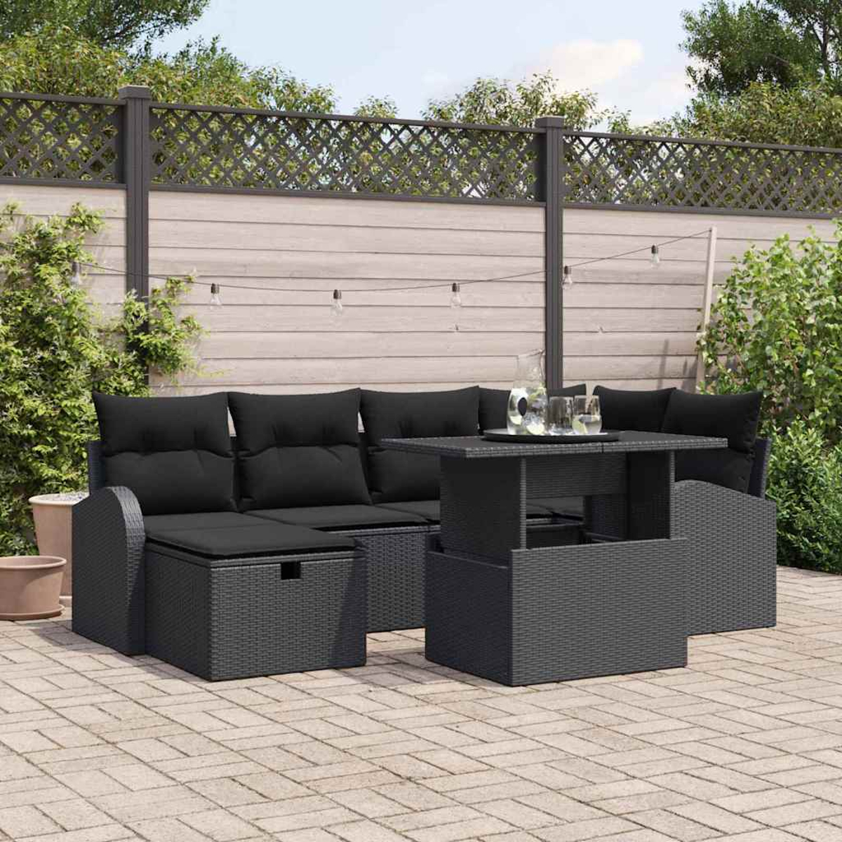 Ein schwarzes Outdoor-Sofaset mit einem Tisch. Im Hintergrund ist ein Zaun, und die Szene spielt sich auf einer Terrasse ab.