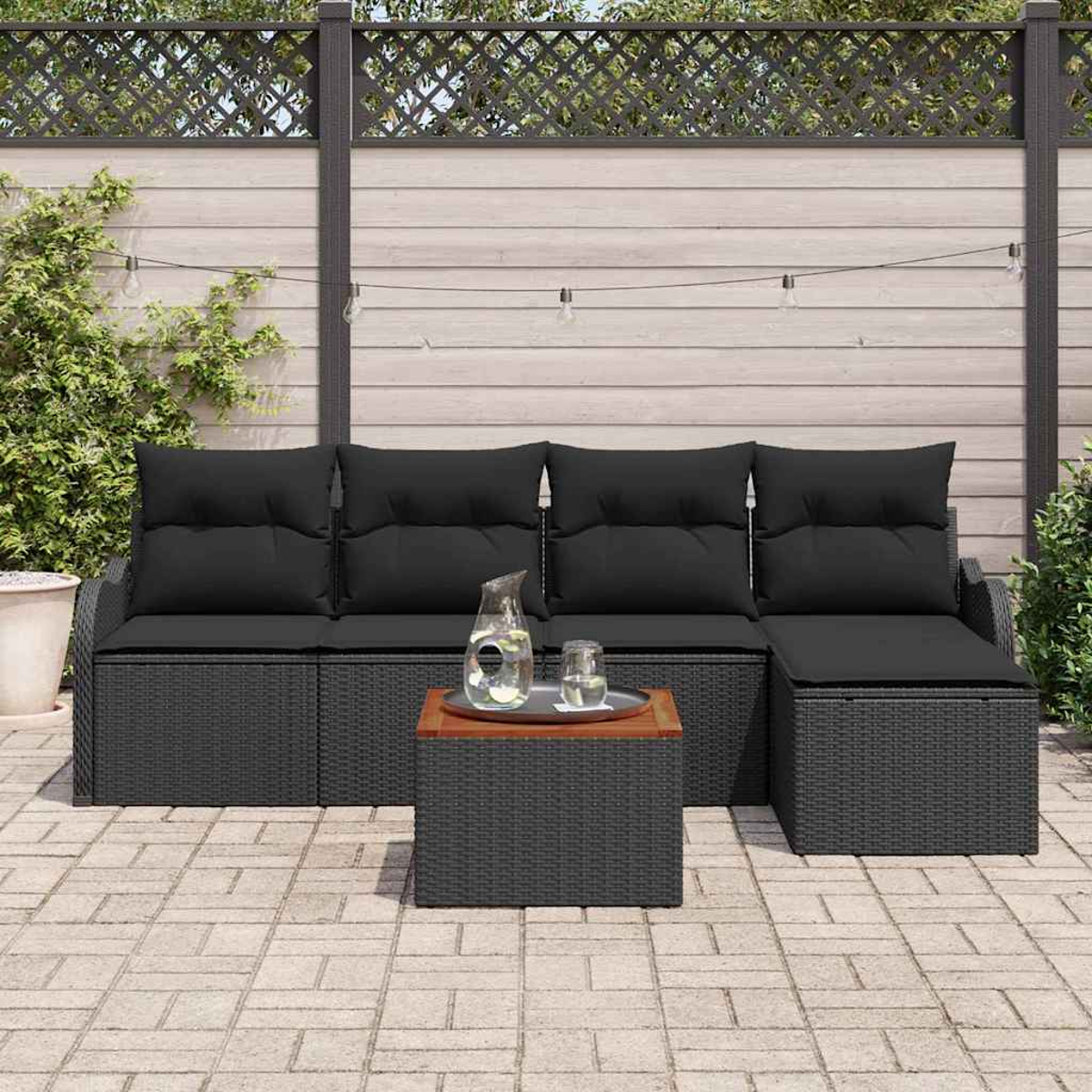 Schwarzes Outdoor-Korbssofa mit Kissen und einem Couchtisch. Auf dem Tisch stehen ein Krug und ein Glas. Der Hintergrund hat einen Zaun.