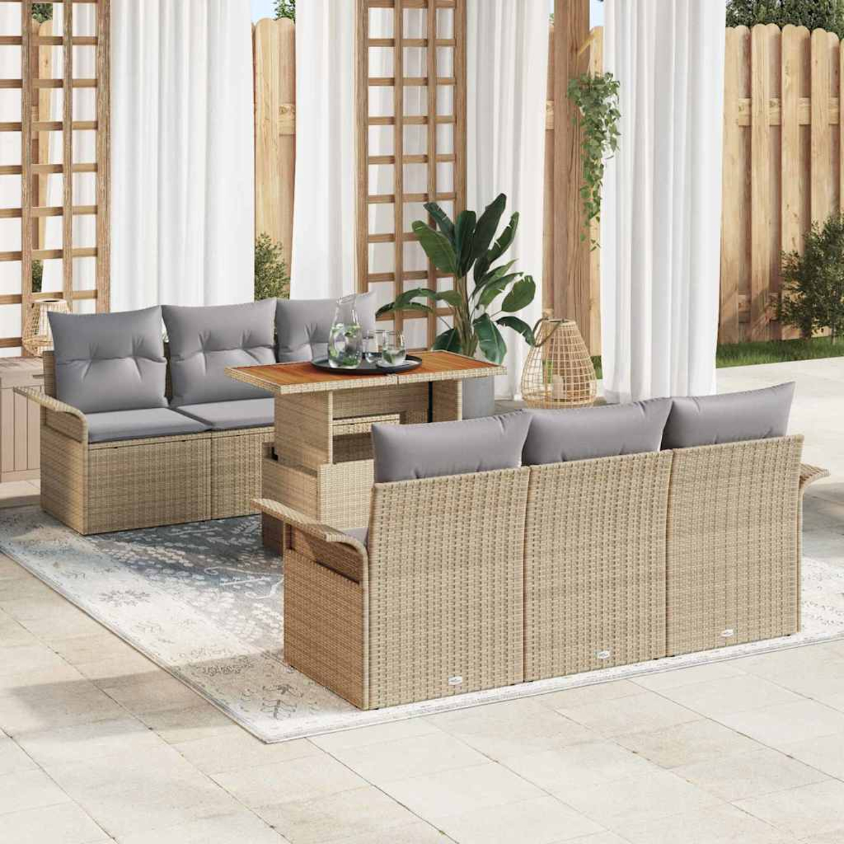 Escena al aire libre con muebles de mimbre y cojines grises. Una mesa con bebidas se encuentra entre dos sofás en un patio con cortinas blancas.