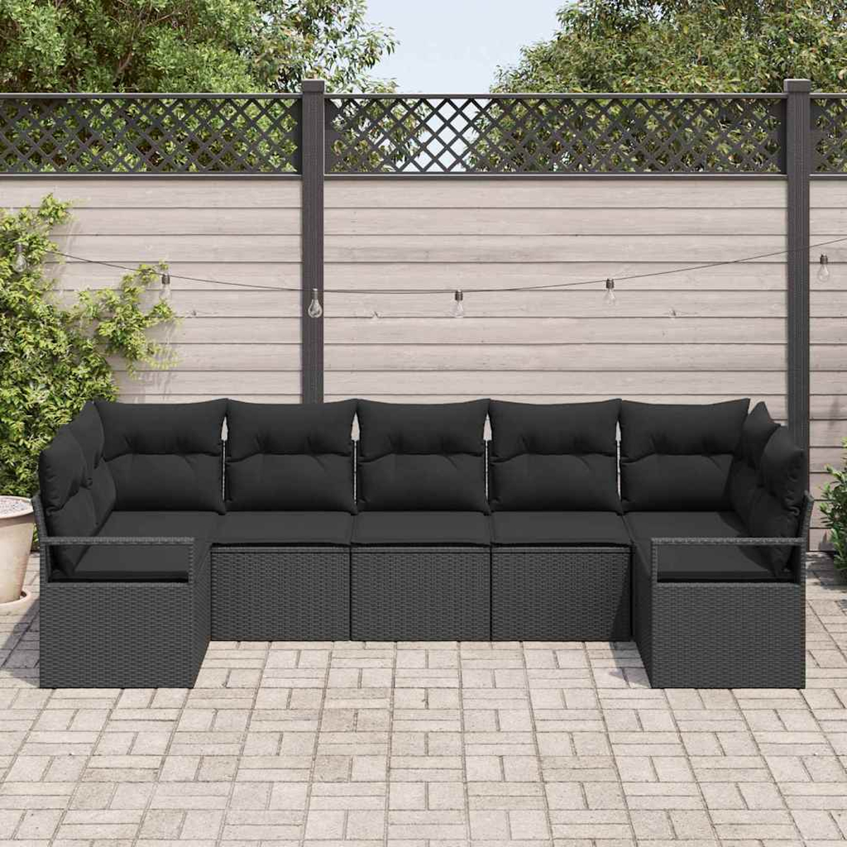 Un sofá seccional de ratán negro para exteriores está en un patio pavimentado. El fondo muestra una valla de madera con plantas trepadoras y luces de cadena.