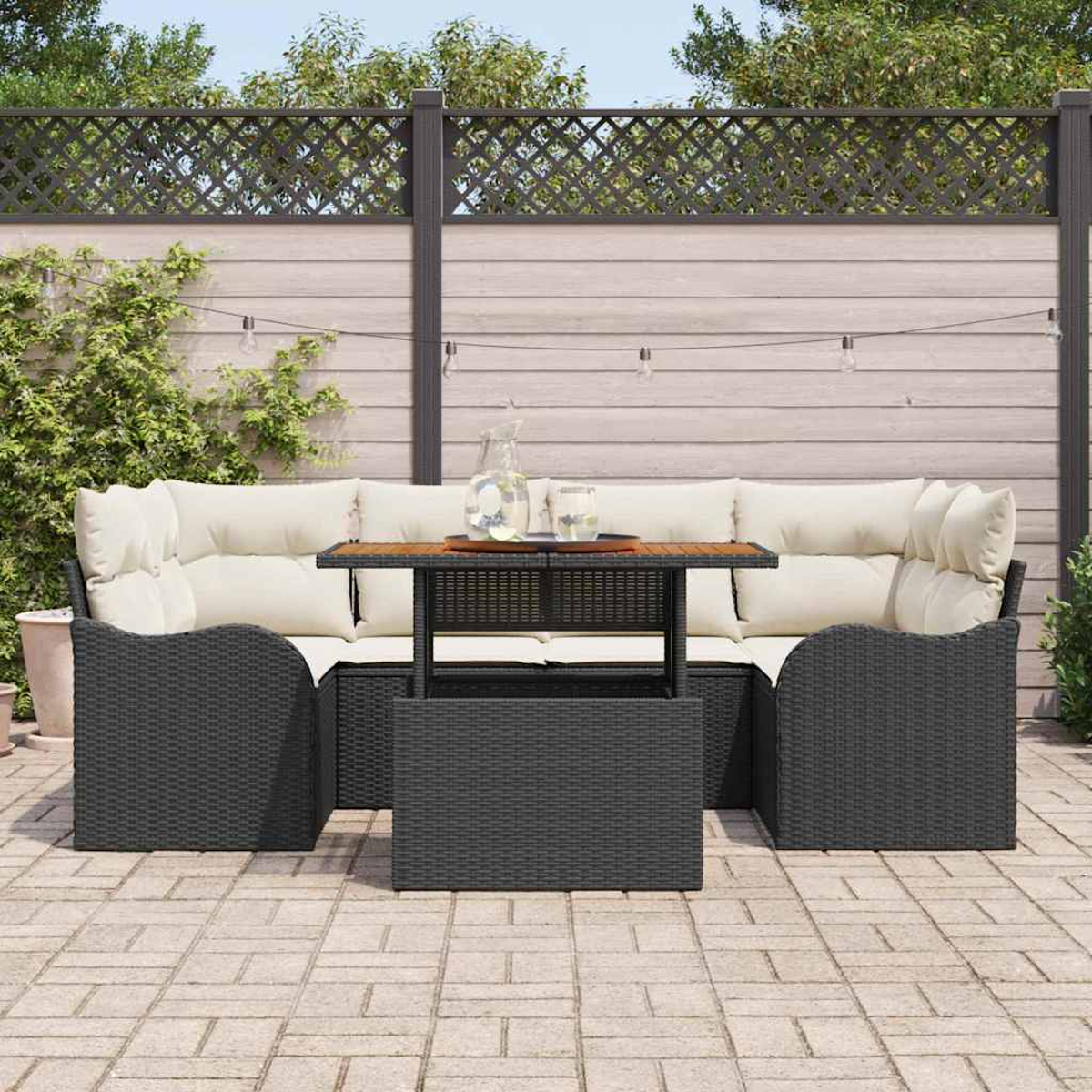 Garten-Sitzgruppe mit Tisch. Dunkle Korbmöbel mit cremefarbenen Kissen. Tisch mit Holzplatte. Hintergrund ist ein Holzzaun.