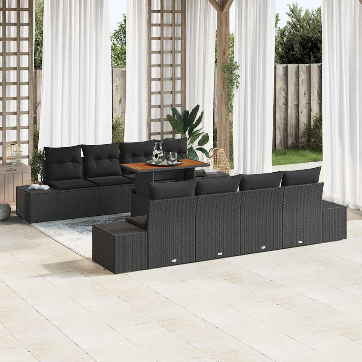 Outdoor-Sitzgruppe mit schwarzen Kissen, einem Holztisch und weißen Vorhängen im Hintergrund. Enthält Pflanzen und dekorative Gegenstände.