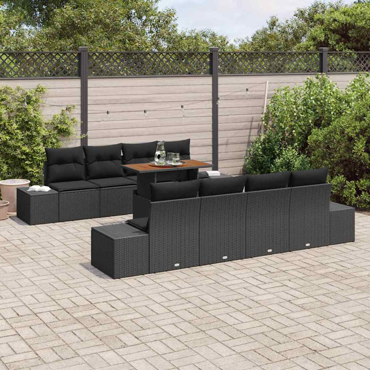 Garten-Terrassenset mit schwarzen Kissen auf einem grauen Korbsessel und Tisch. Backstein-Patio und Holzzaun im Hintergrund.