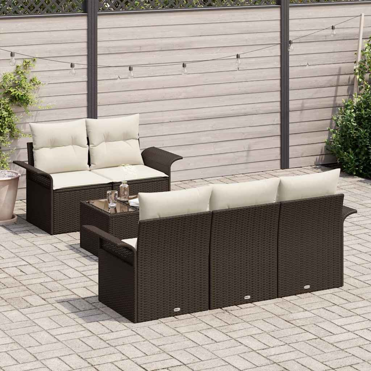 Gartenmöbel-Set. Braunes Korbsessel und -sofa mit cremefarbenen Kissen, Glastisch. Holzzaun-Hintergrund, Lichterketten und Pflasterboden.