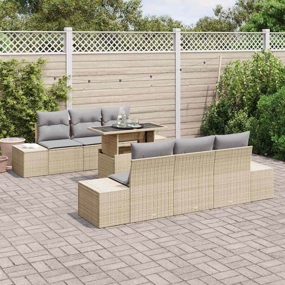 Gartenmöbel-Set aus Korbgeflecht mit grauen Kissen auf einer Ziegelpflasterung. Ein Tisch mit Gläsern und einem Krug steht in der Mitte.